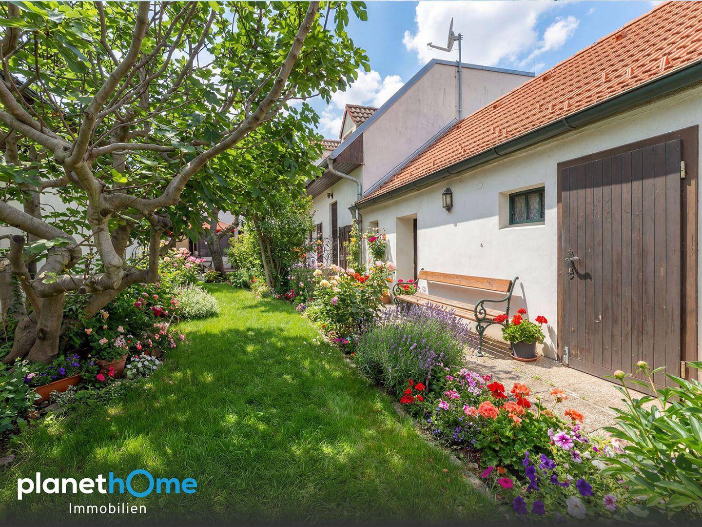 Gepflegter Garten mit Rasenfläche, Blumenbeeten und einem Sitzbank.