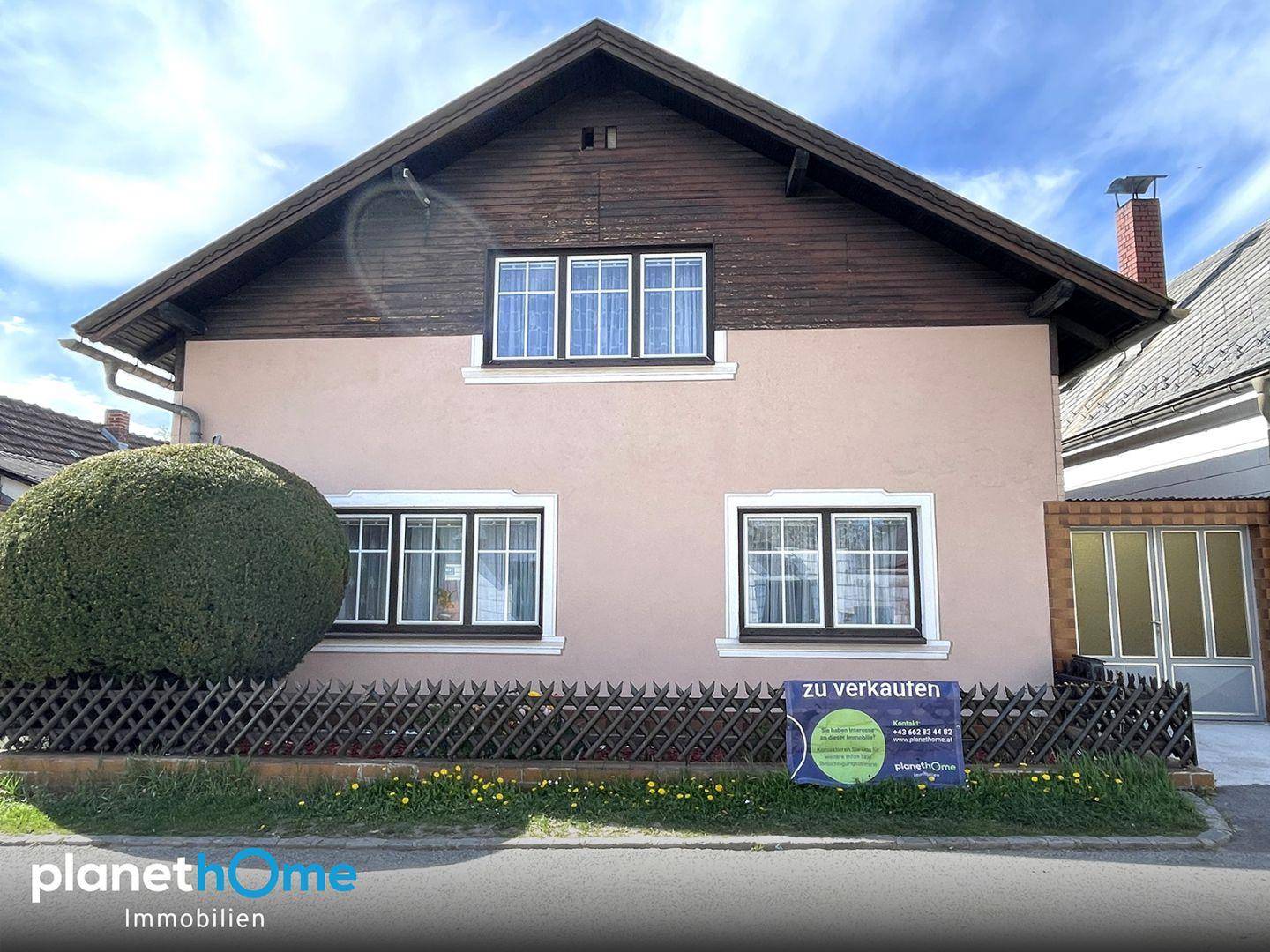 Vorderansicht eines Einfamilienhauses mit rosafarbener Fassade, Holzdachgiebel und kleinem Vorgarten.
