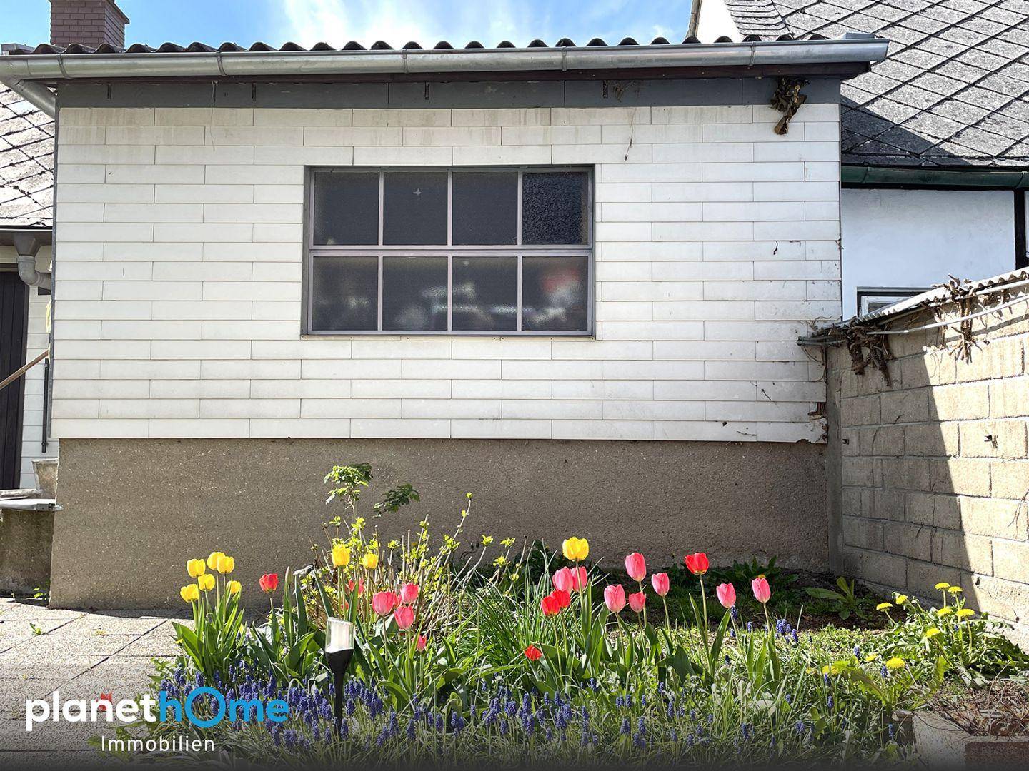 Seitenansicht des Gebäudes mit einem gepflegten Gartenbereich und blühenden Tulpen.
