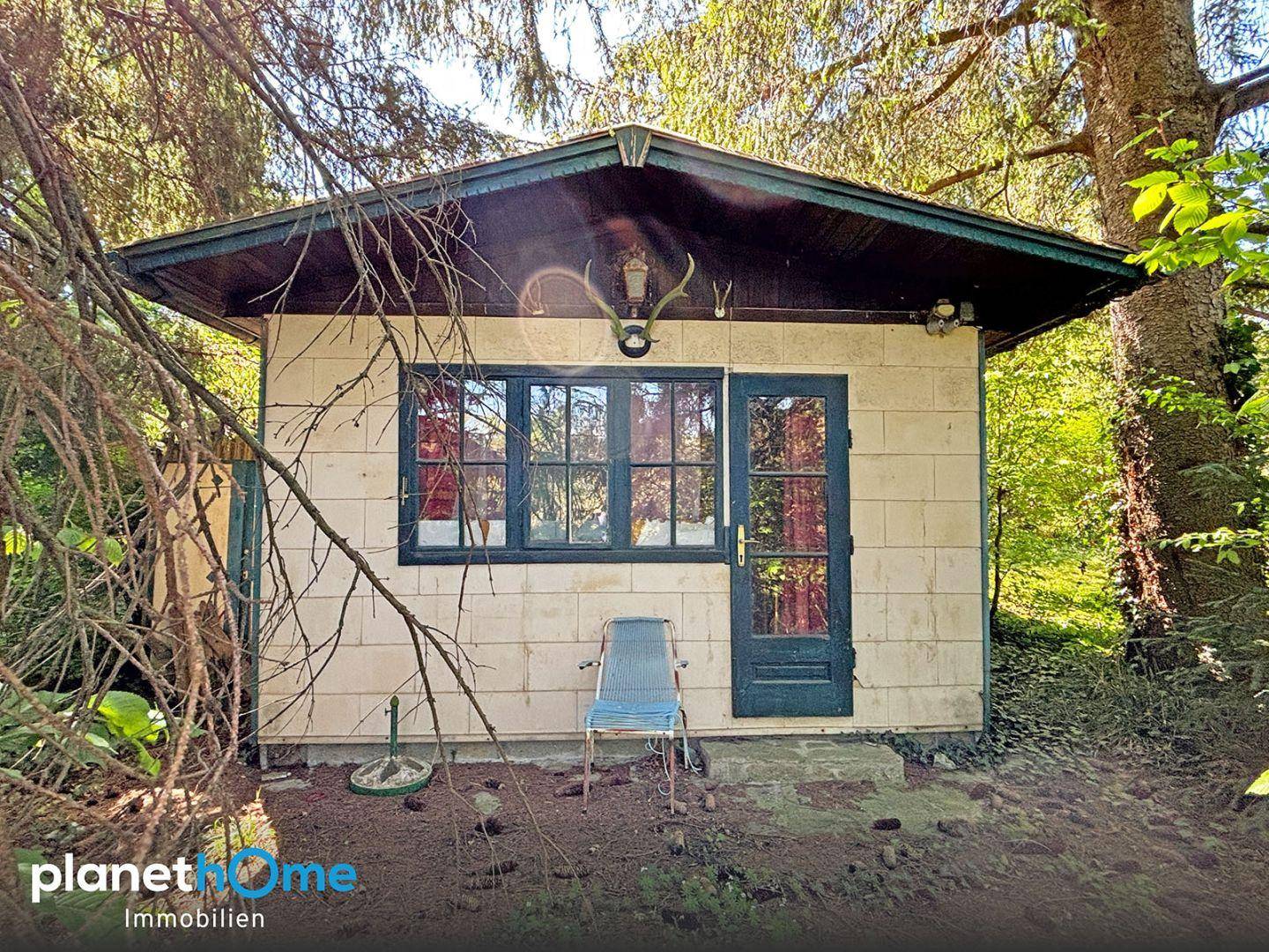 Rustikales Gartenhaus umgeben von Bäumen mit einer Hirschgeweih-Dekoration über der Tür.
