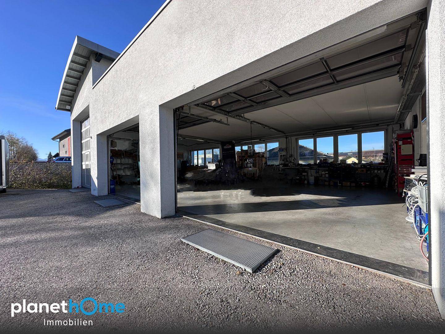 Geräumige Werkstatt oder Garage mit offenem Tor und viel Tageslicht, ideal für Fahrzeuge.