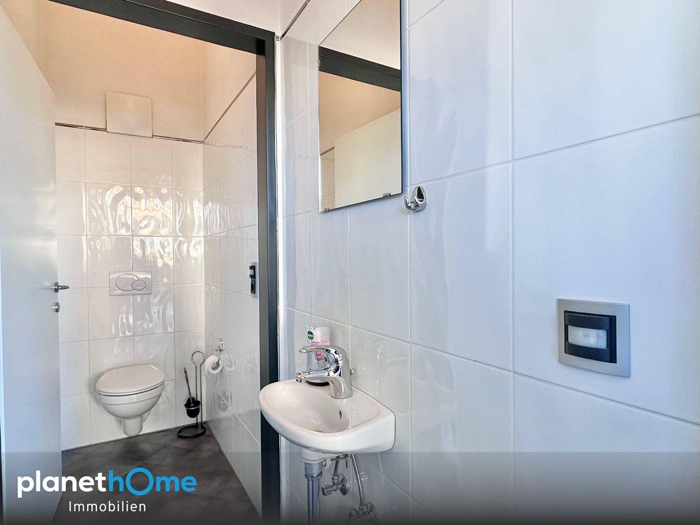 Modernes Gäste-WC mit weißen Fliesen, wandmontierter Toilette und kleinem Waschbecken.