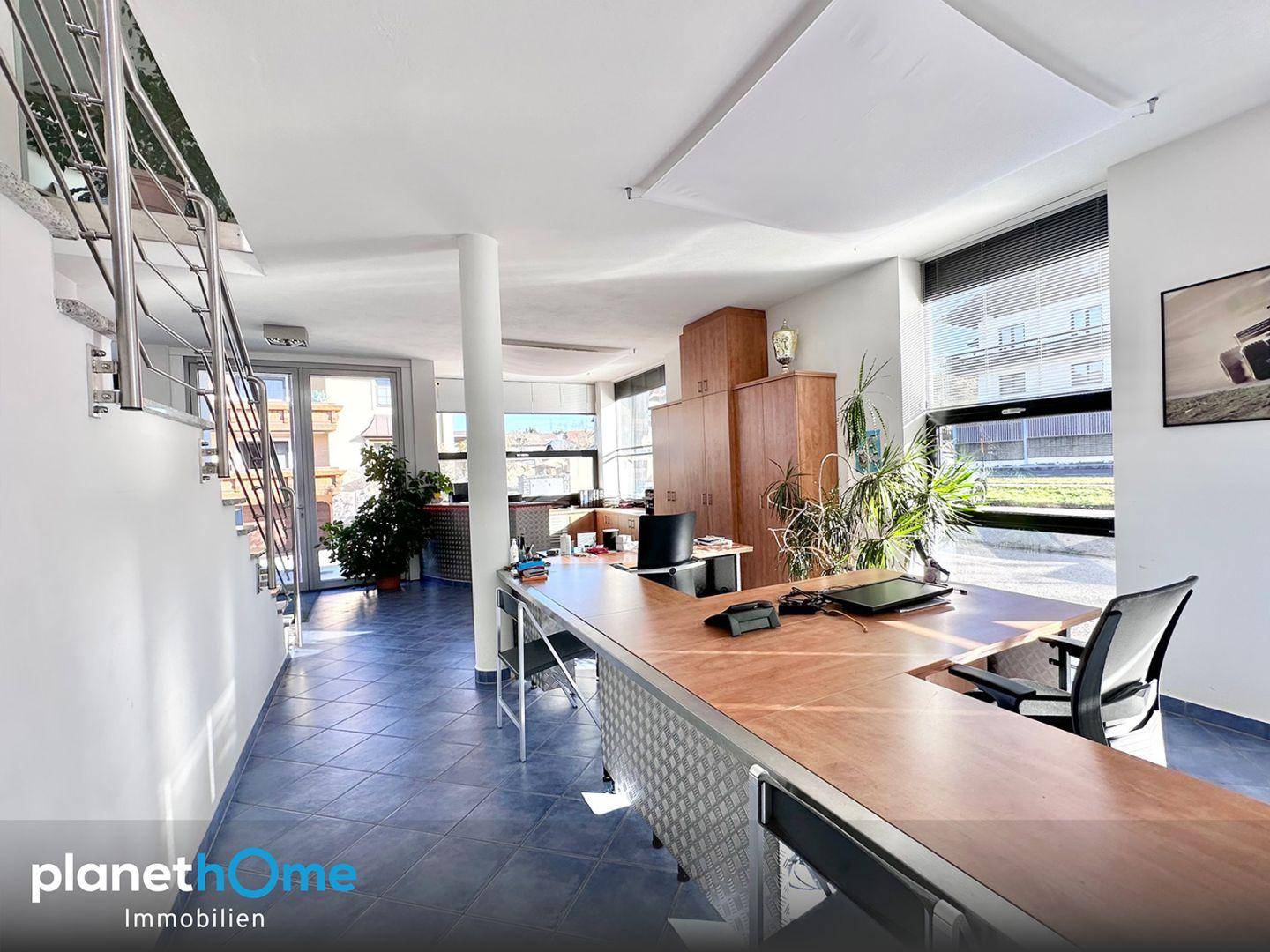 Helles und offenes Büro mit mehreren Arbeitsplätzen, Pflanzen und einer modernen Treppe.