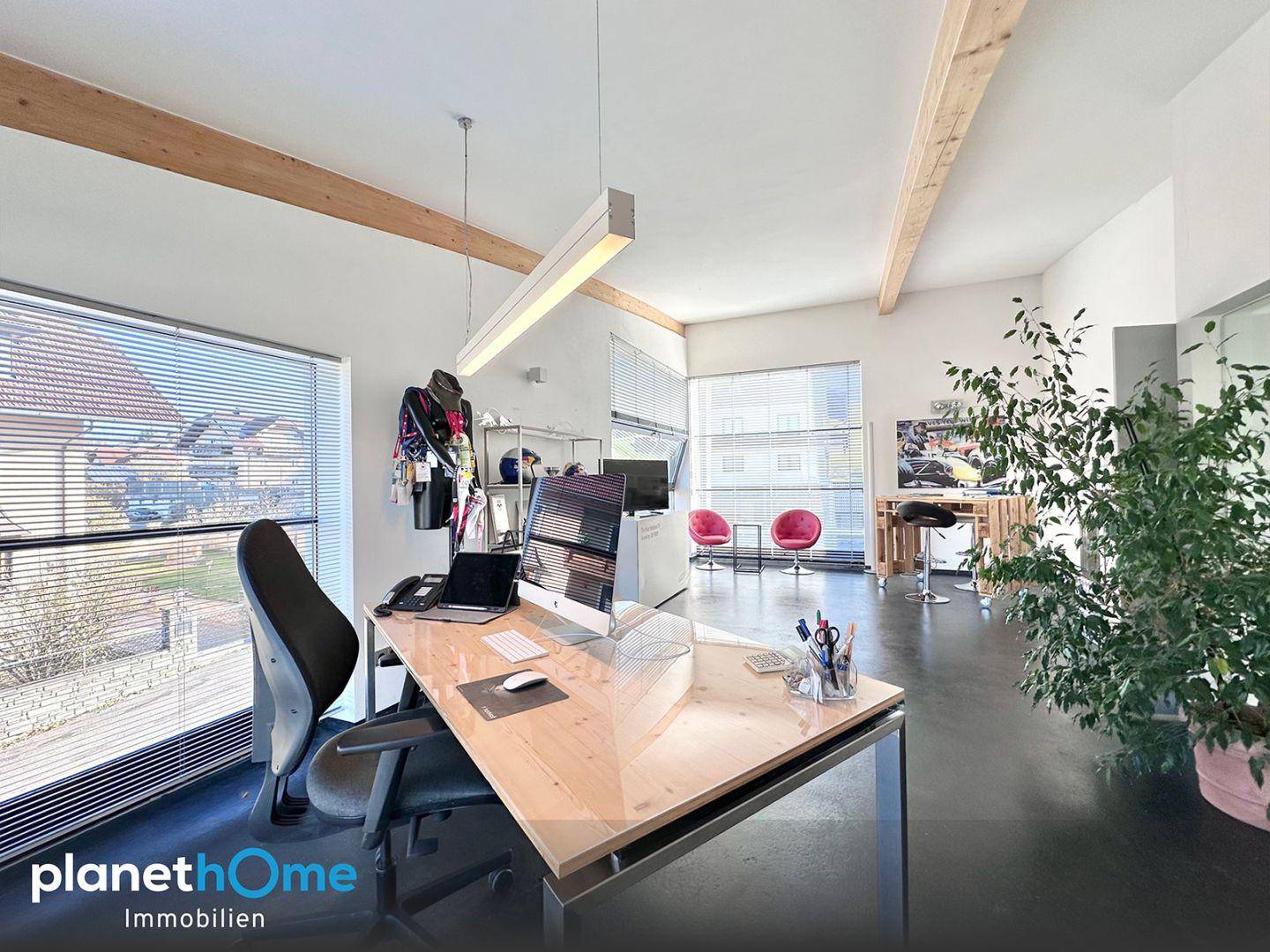 Helles Büro im Obergeschoss mit sichtbaren Holzbalken, großen Fenstern und modernen Arbeitsplätzen.