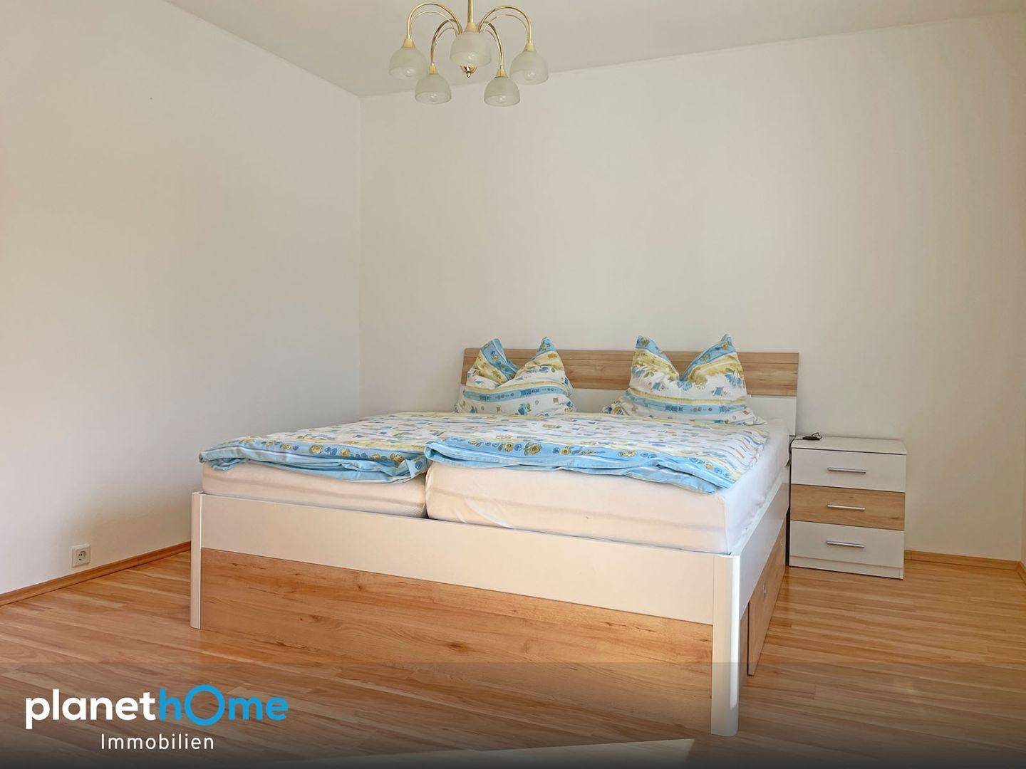 Helles Schlafzimmer mit Holzbett und Nachttischen, ausgestattet mit Parkettboden.