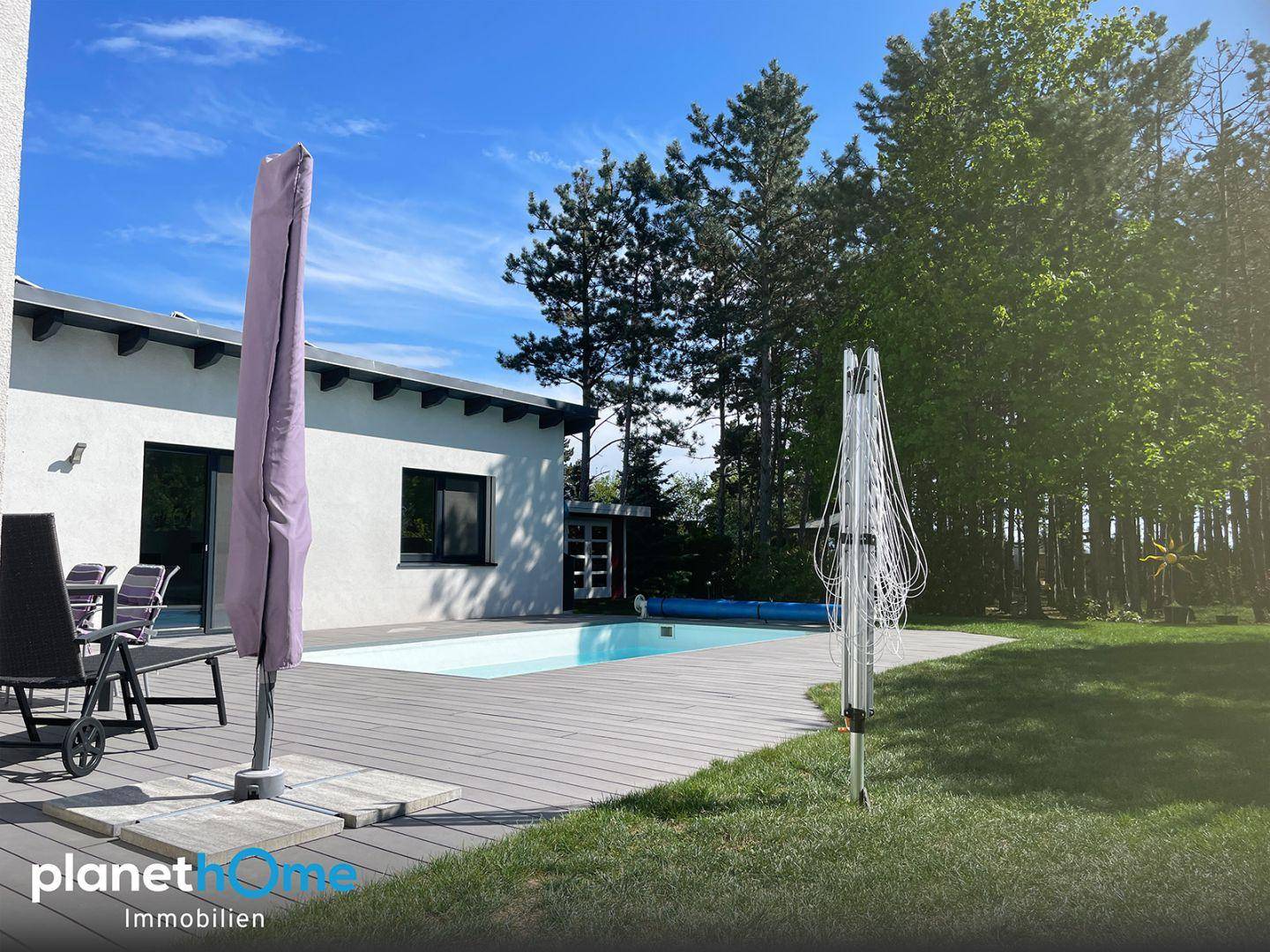 Weitläufiger Gartenbereich mit Pool, Sonnenterrasse und viel Grün unter blauem Himmel.