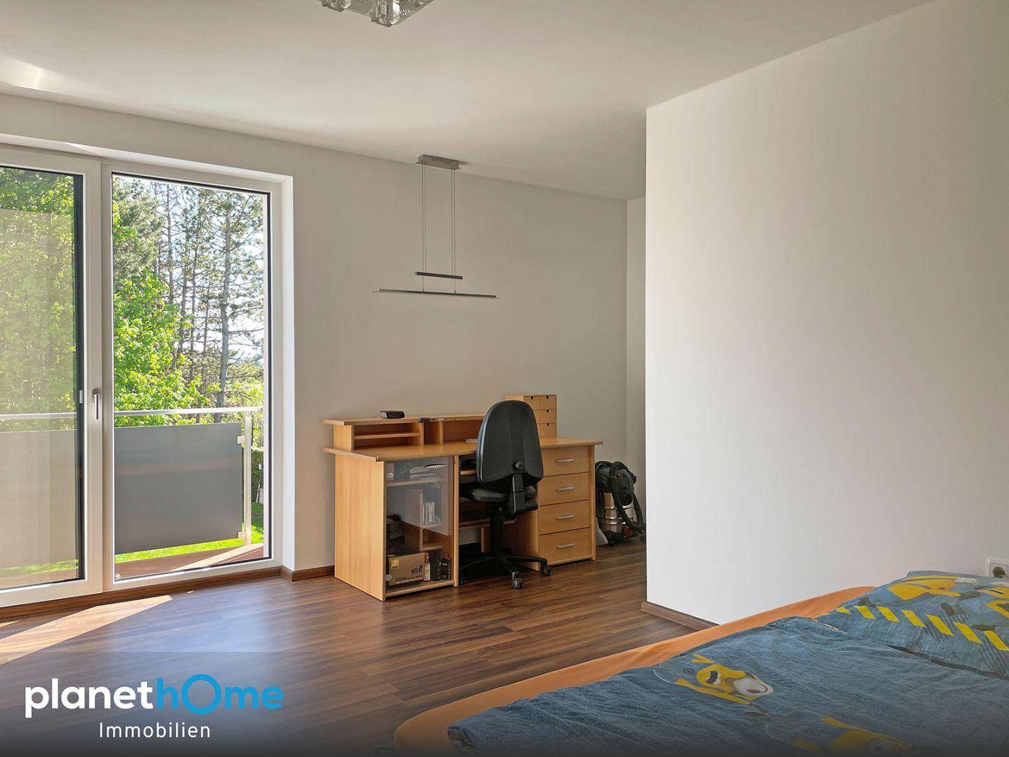 Schlafzimmer mit Schreibtisch, Holzboden und direktem Zugang zu einem Balkon.