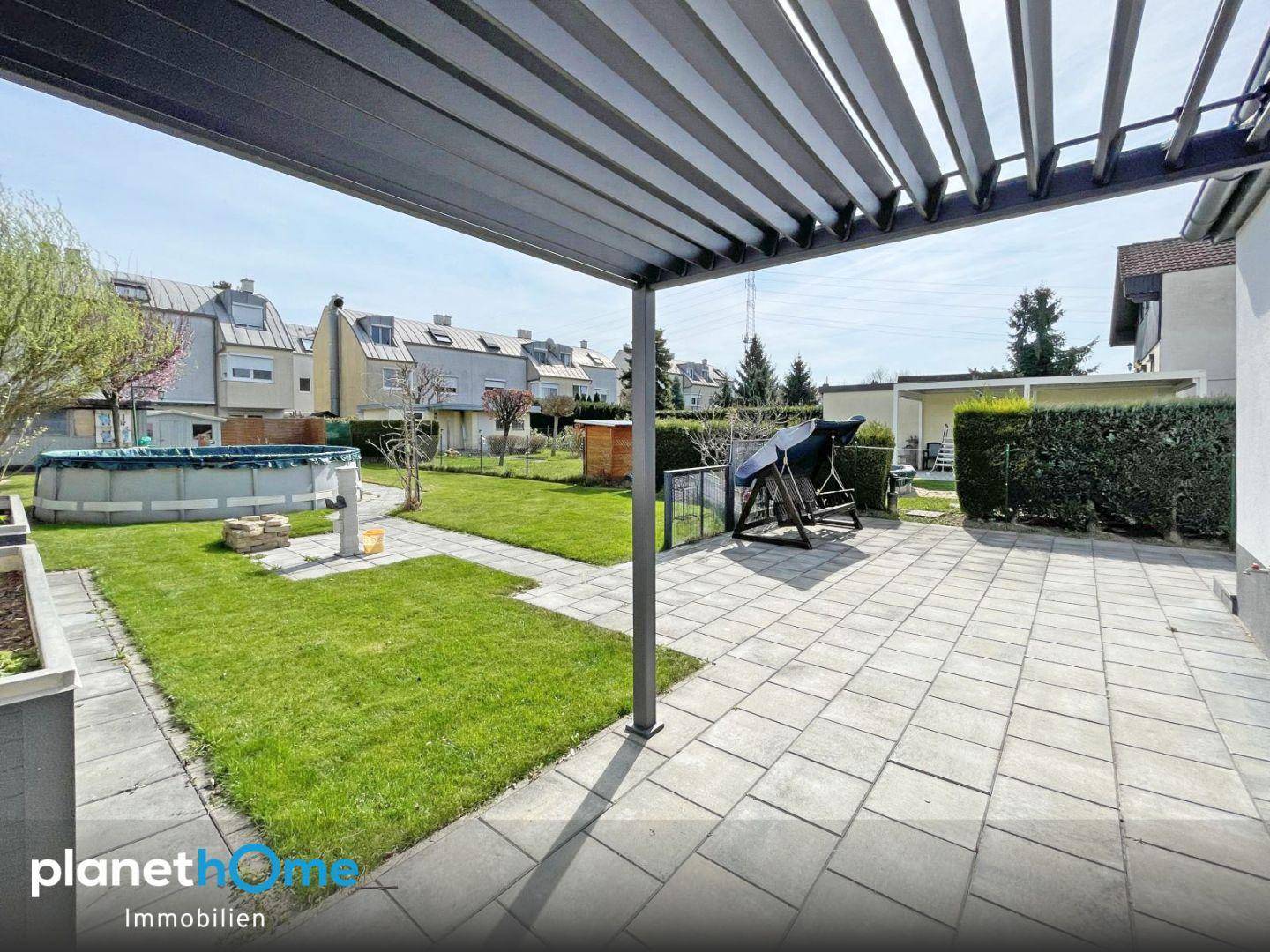 Große gepflasterte Terrasse unter einer Pergola mit Blick auf den Garten und Pool.