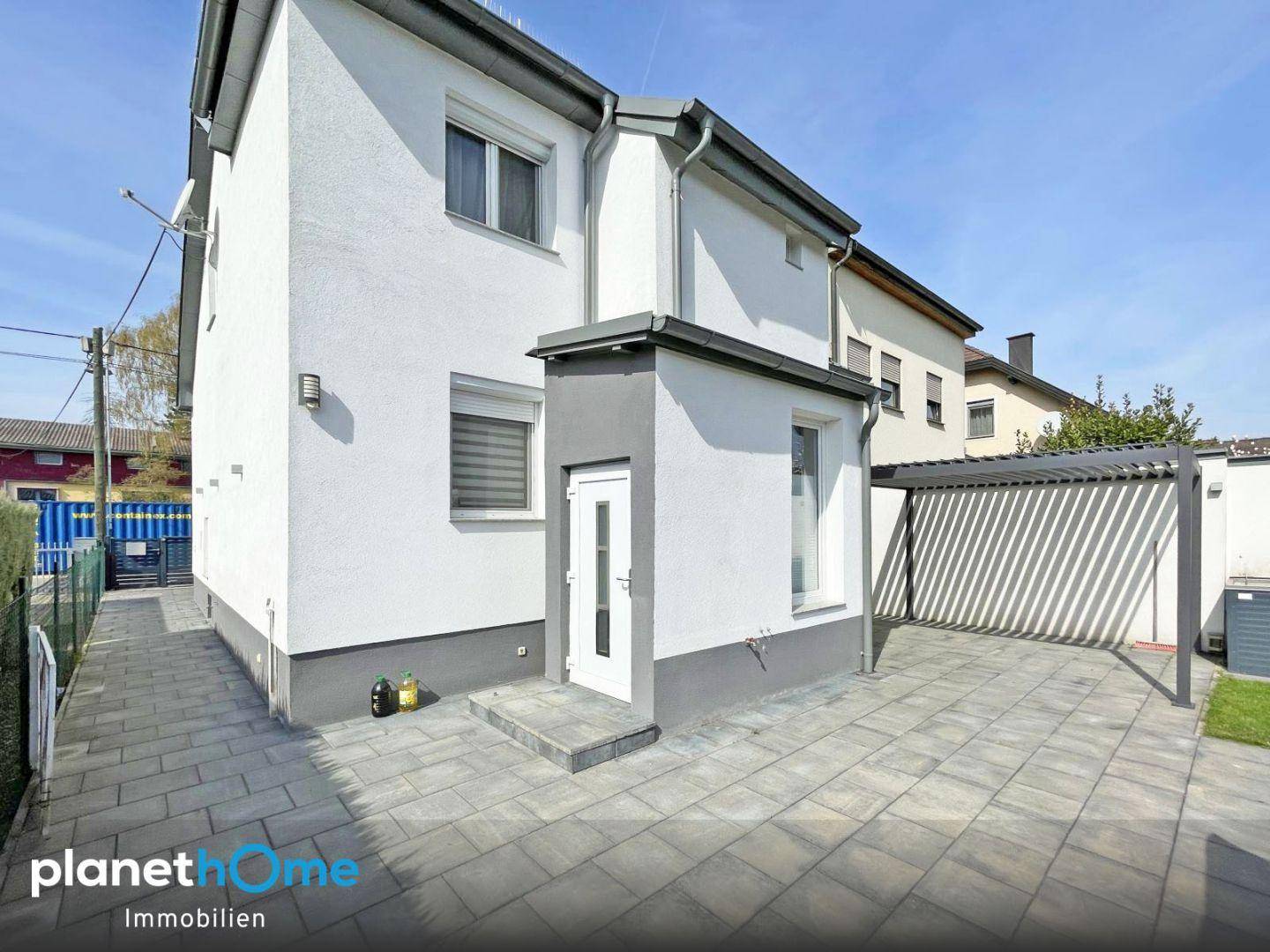 Seitenansicht des Hauses mit Eingangsbereich, gepflastertem Hof und einem Carport.