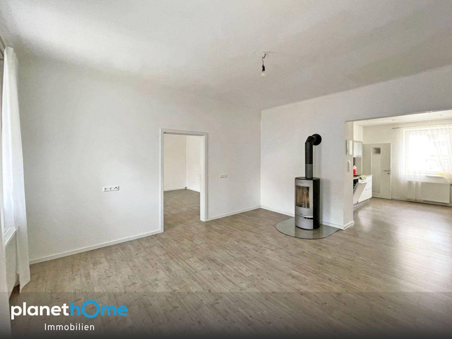 Geräumiges Wohnzimmer mit modernem Kaminofen, Laminatboden und Zugang zur Küche.