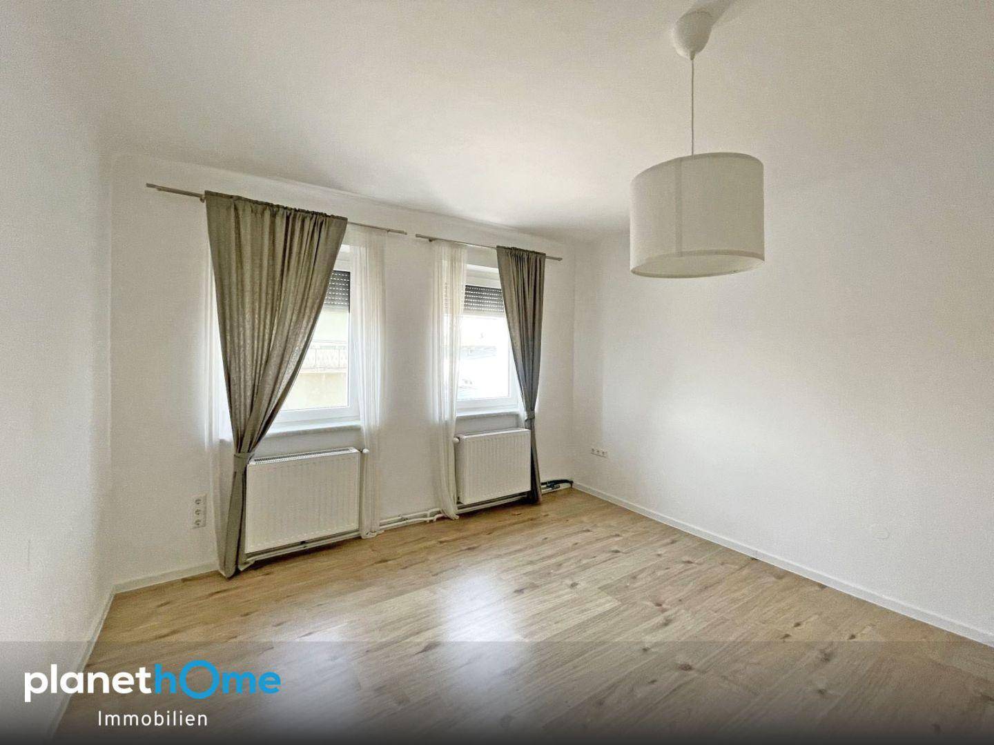 Geräumiges Schlafzimmer mit Laminatboden, weißen Wänden und Vorhängen.
