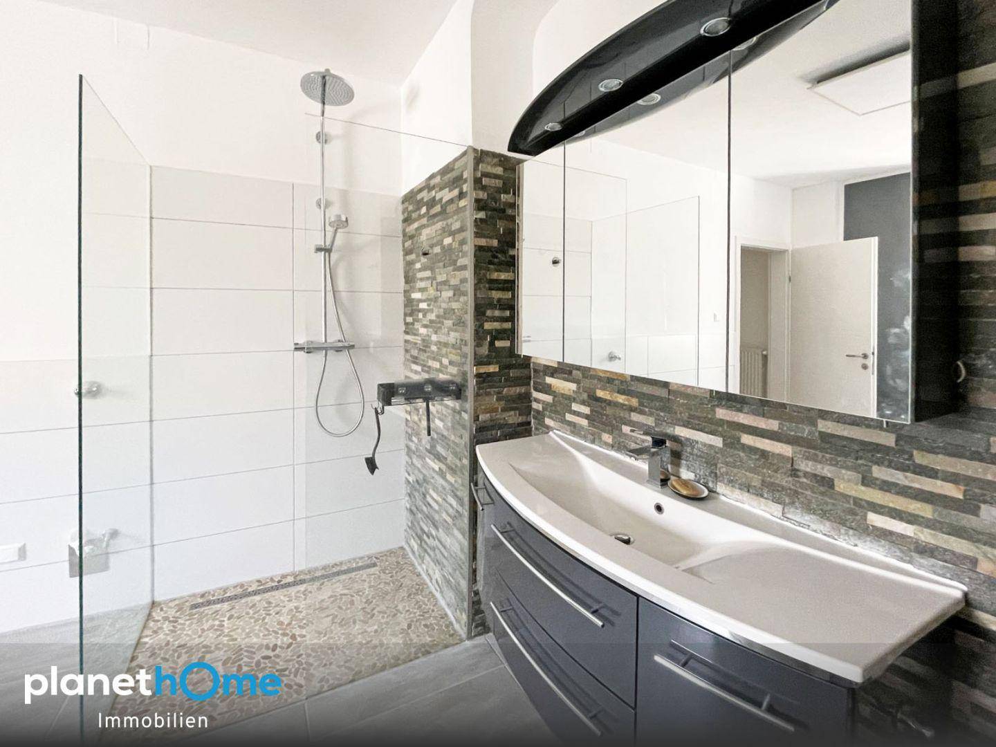 Modernes Badezimmer mit begehbarer Dusche, stilvollem Waschbecken und Steinakzentwand.