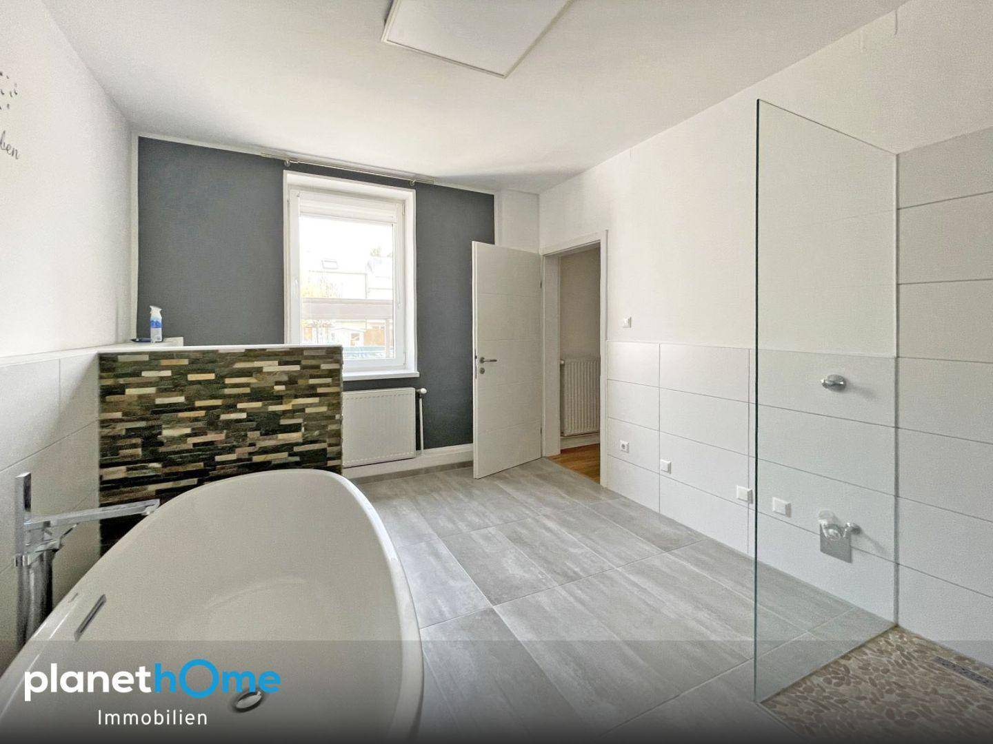Geräumiges Badezimmer mit moderner Badewanne, begehbarer Dusche und Fenster.