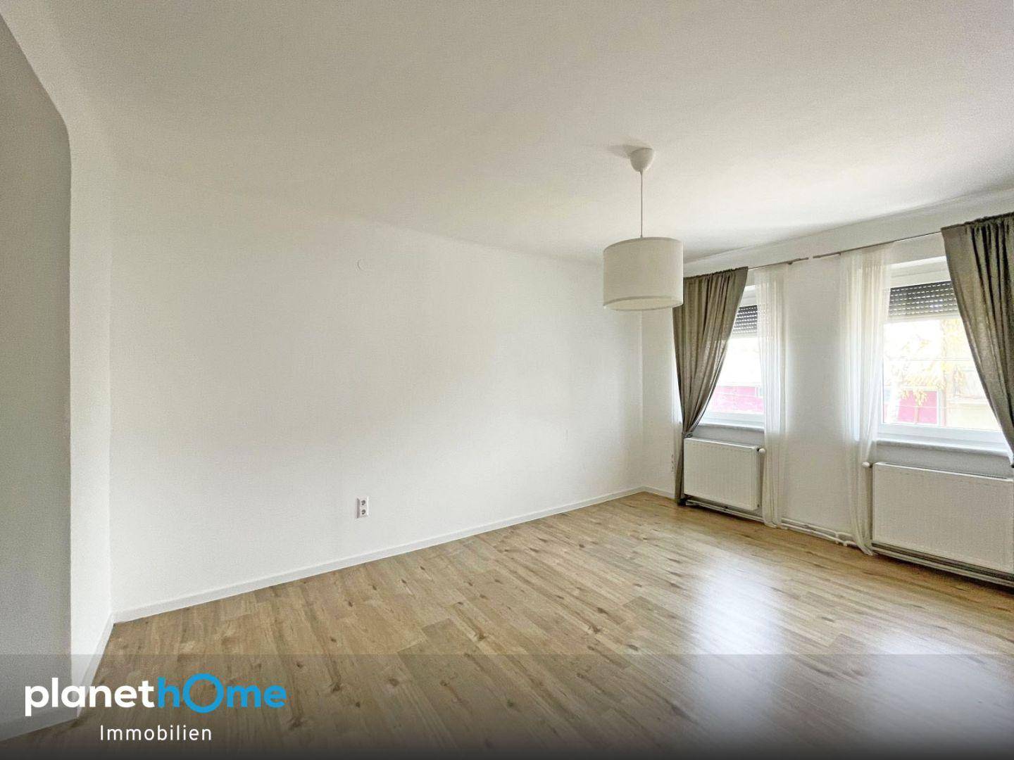 Helles Schlafzimmer mit Laminatboden, weißen Wänden und zwei Fenstern.
