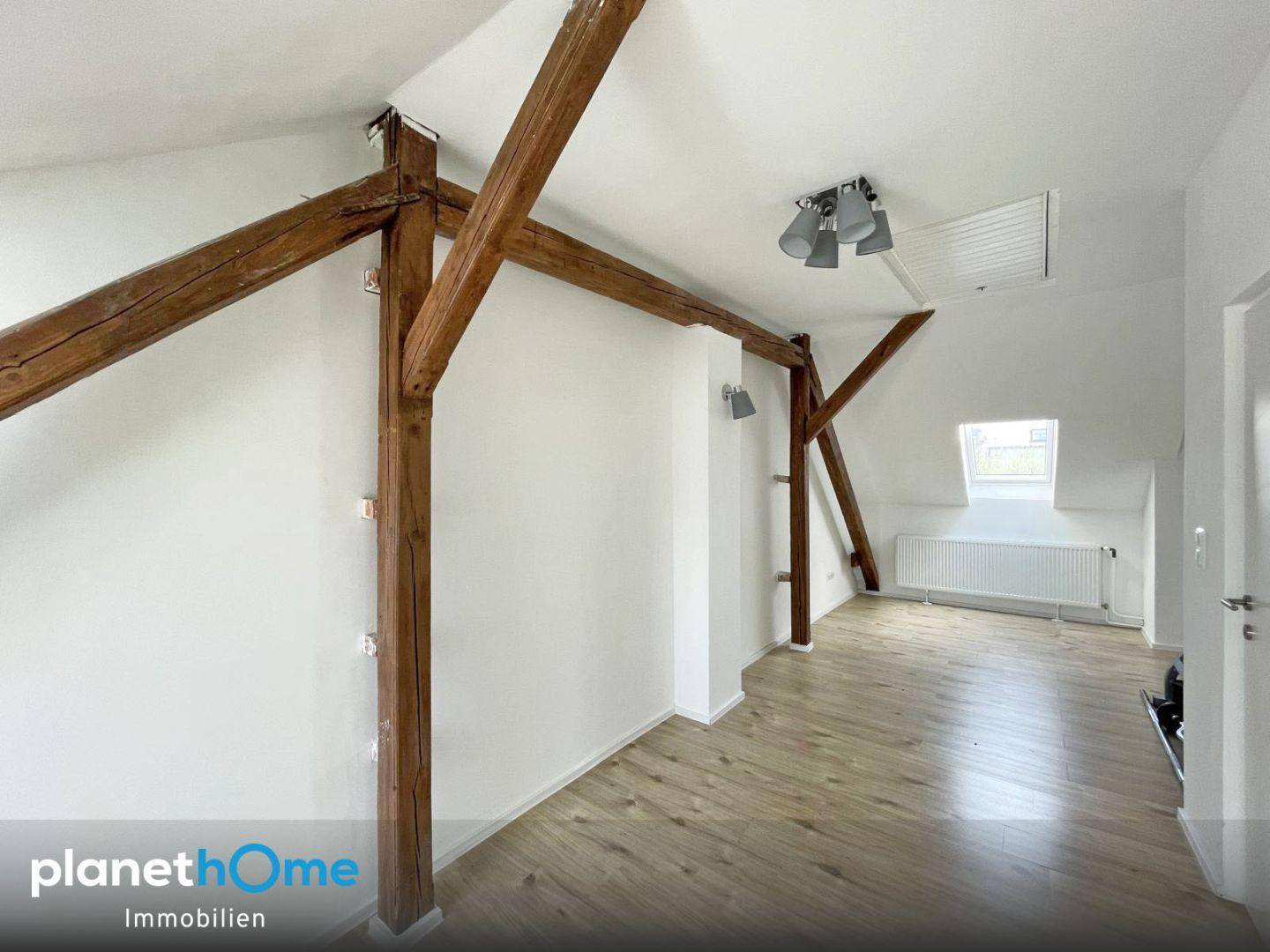 Helles Dachzimmer mit sichtbaren Holzbalken, weißen Wänden und modernem Laminatboden.