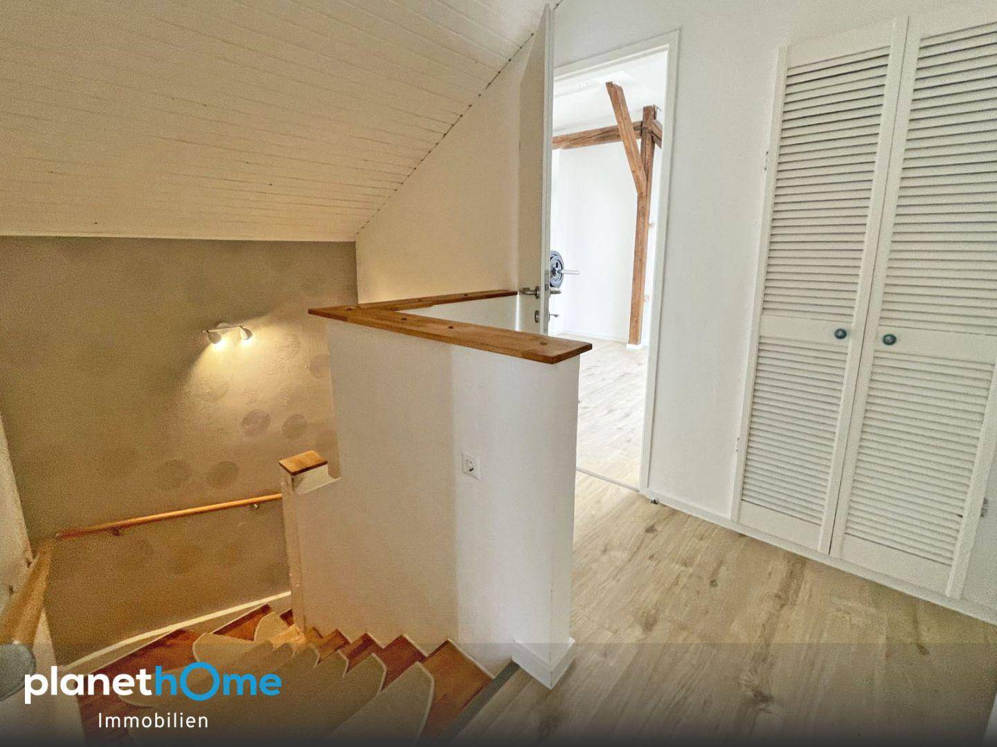 Treppenhaus mit Holzstufen und hellem Laminatboden, führt zu einem Raum mit Holzbalken.