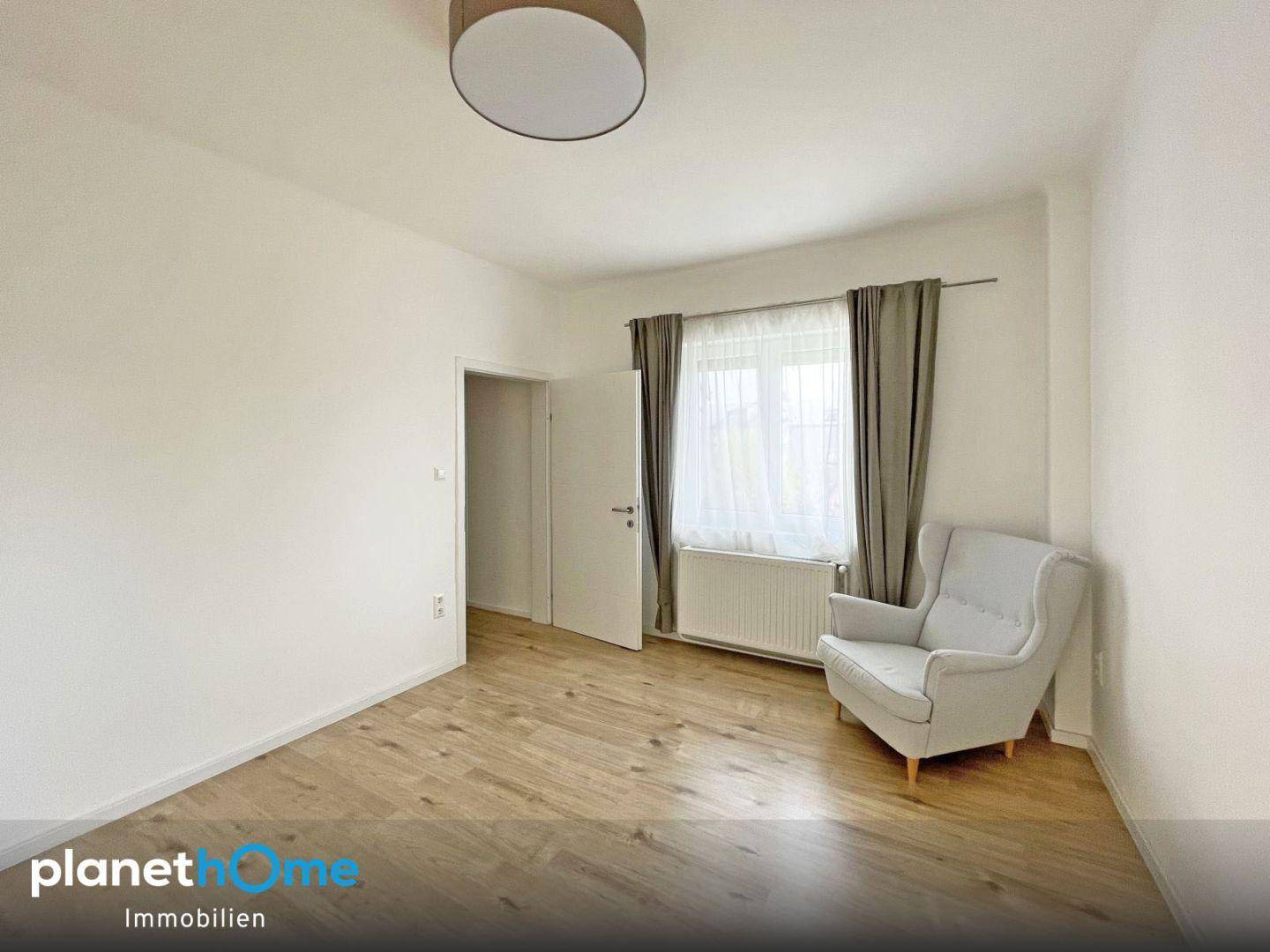 Gemütlicher Raum mit Laminatboden, Sessel und Fenster mit Vorhang.