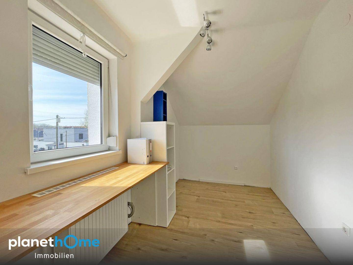 Helles Dachzimmer mit Schreibtischbereich, Laminatboden und Dachschräge.