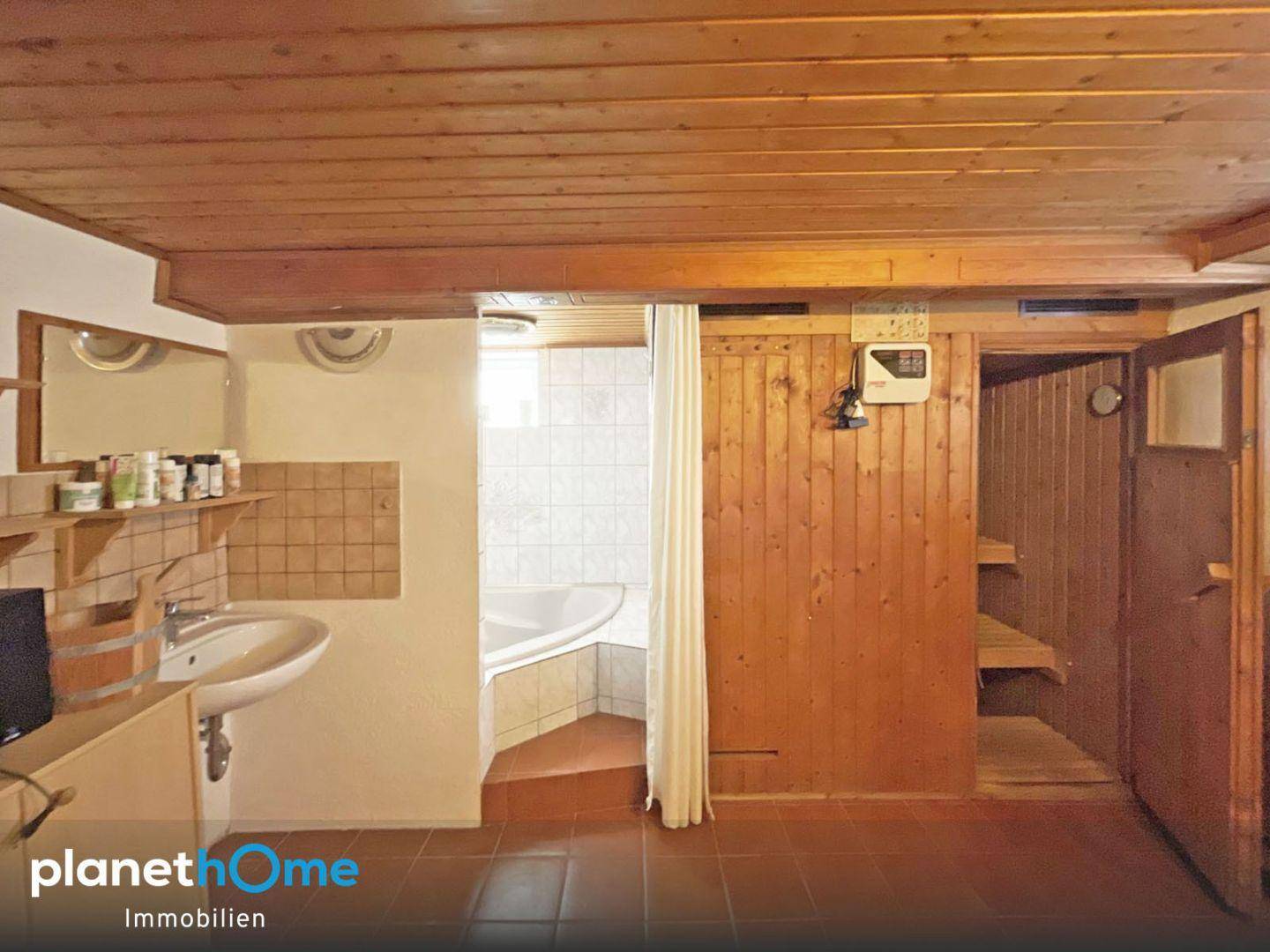 Badezimmer mit Eckbadewanne, Waschbecken und einer integrierten Holzsauna unter einer Holzdecke.