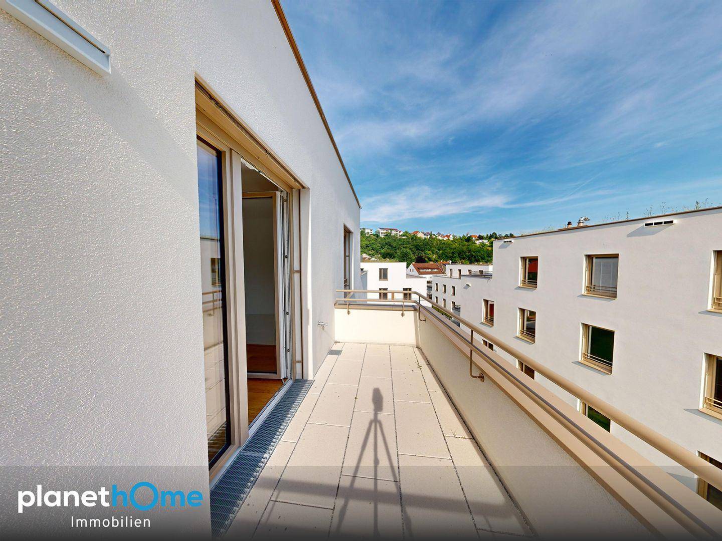 Langer Balkon mit Fliesenboden und weitem Blick auf die umliegende Bebauung und Natur.
