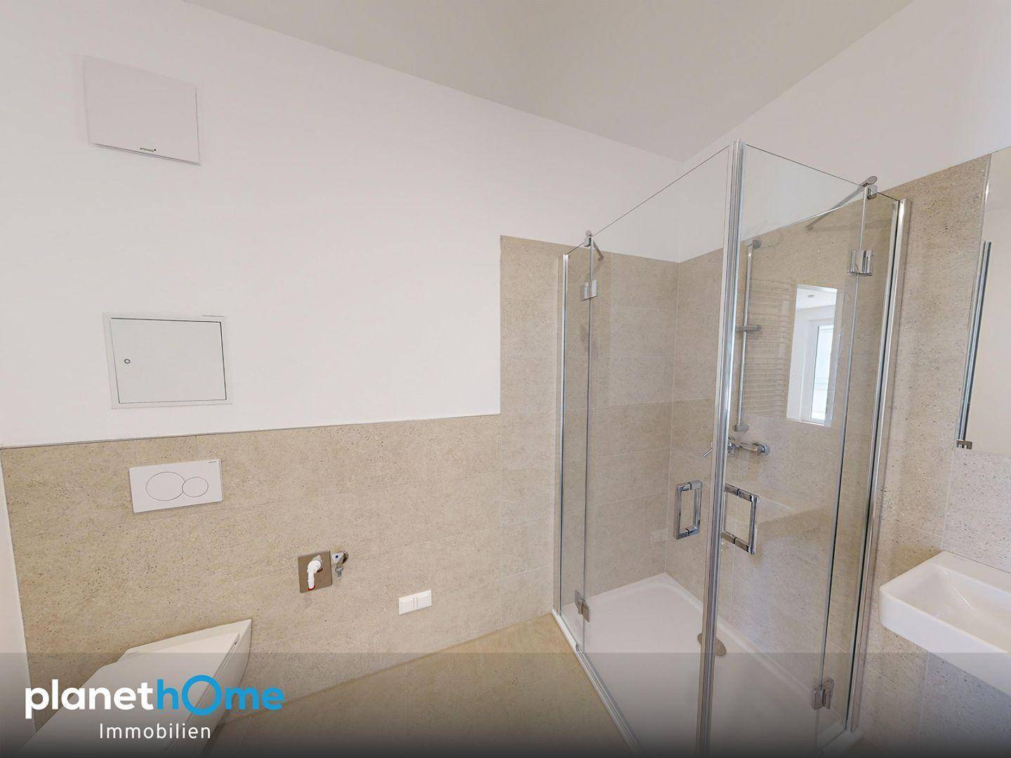 Modernes Badezimmer mit Duschkabine, Wand-WC und beigefarbenen Fliesen an Wänden und Boden.