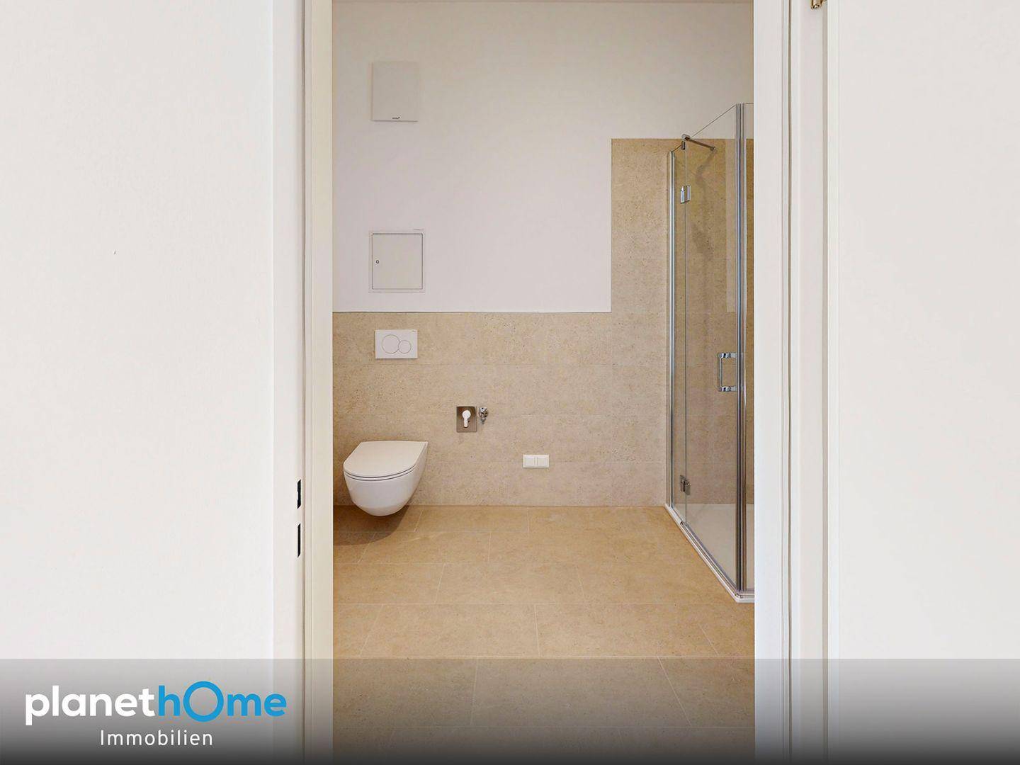 Badezimmer mit Duschkabine und Wand-WC, sichtbar durch den Türrahmen, in neutralen Farbtönen.