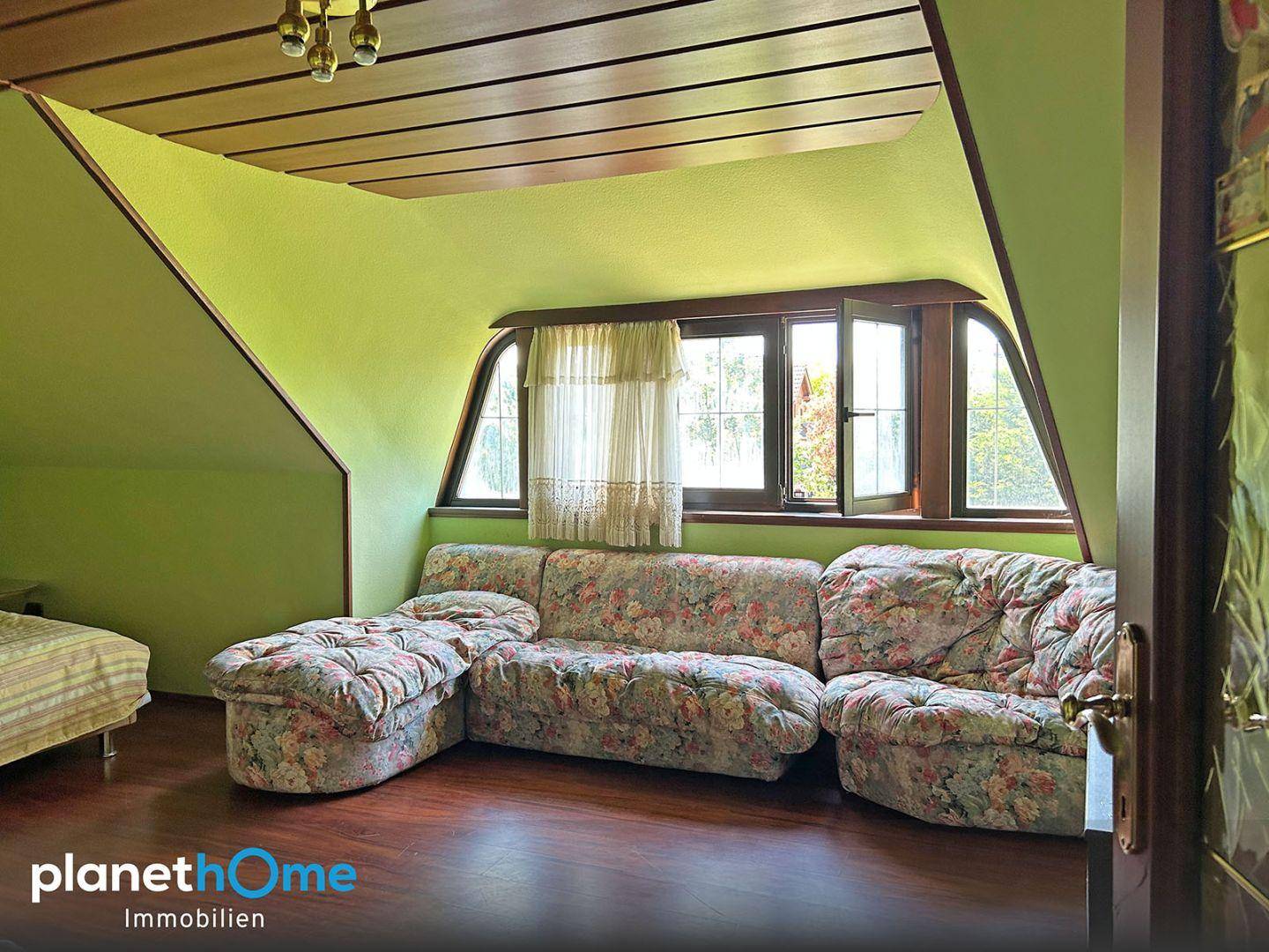 Dachgeschosszimmer mit schrägen Wänden, floralem Sofa und Fenstern.