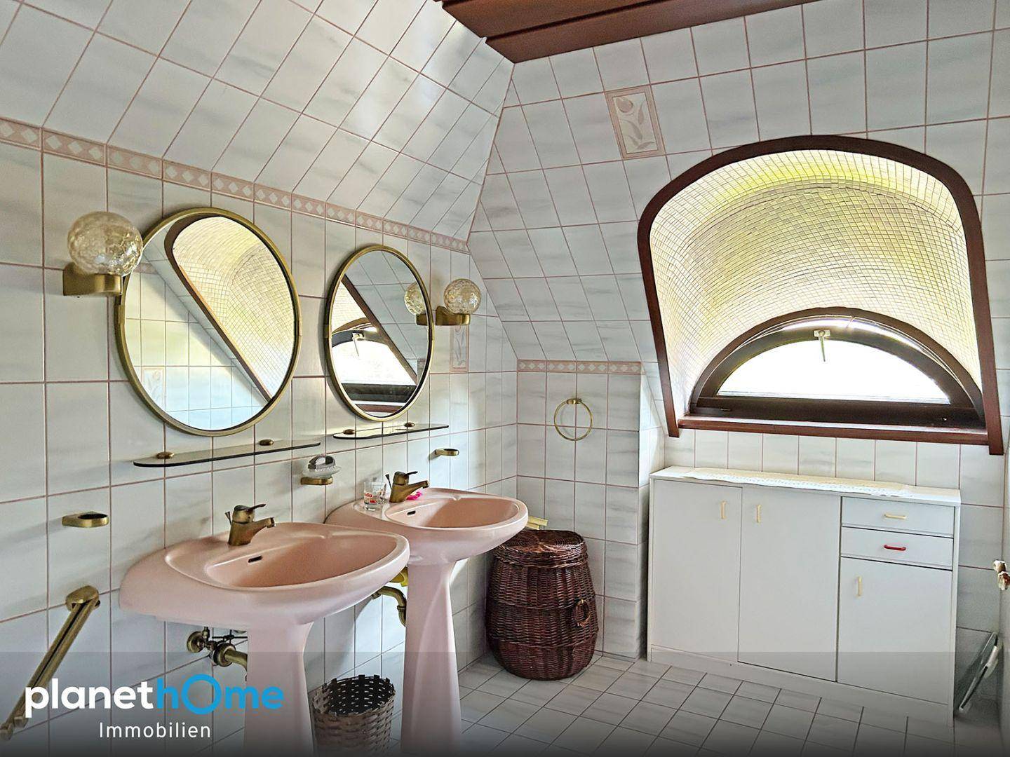 Badezimmer mit rosa Waschbecken, weißen Fliesen und einem dekorativen Bogenfenster.