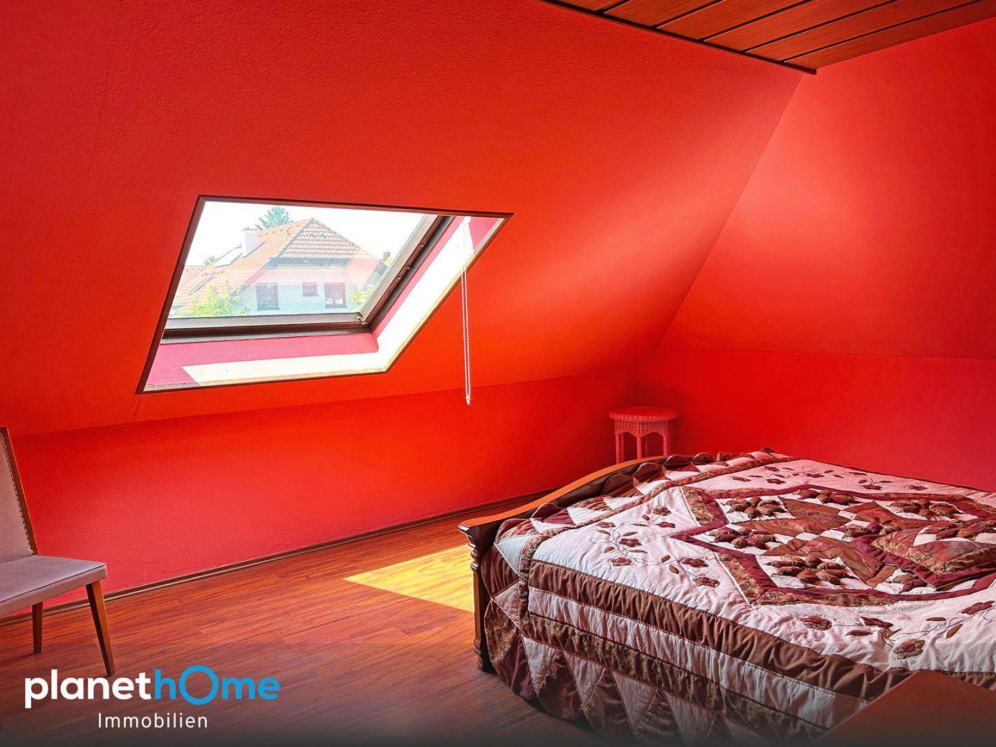 Schlafzimmer im Dachgeschoss mit roten Wänden, Bett und Dachfenster.