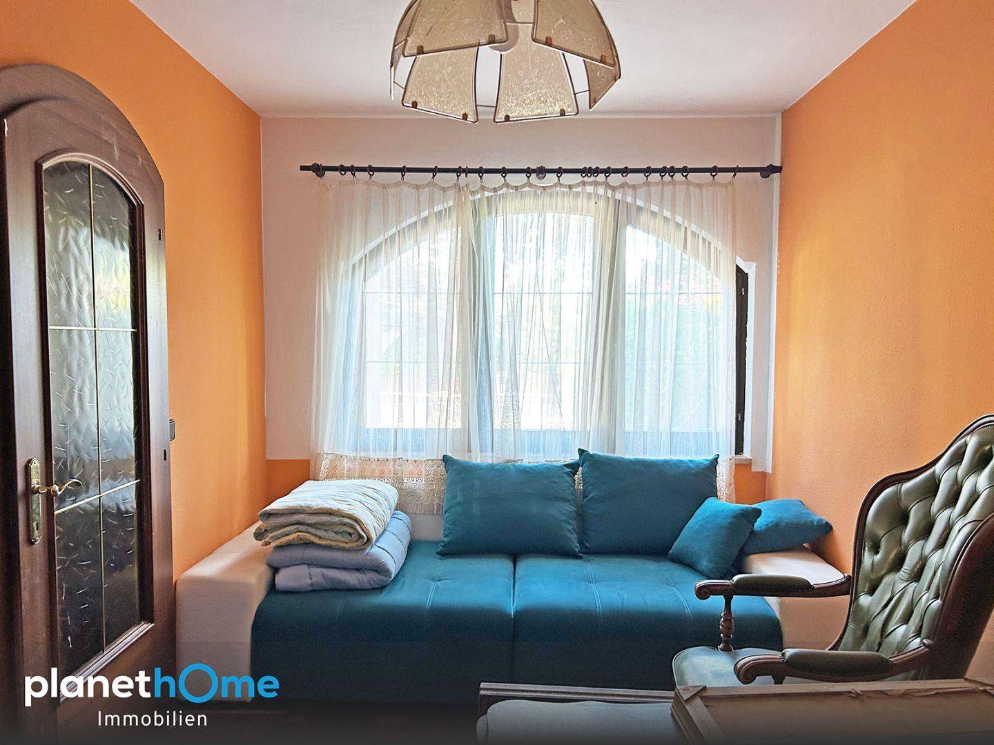 Heller Raum mit blauem Sofa, Sessel und großem Bogenfenster mit Vorhängen.