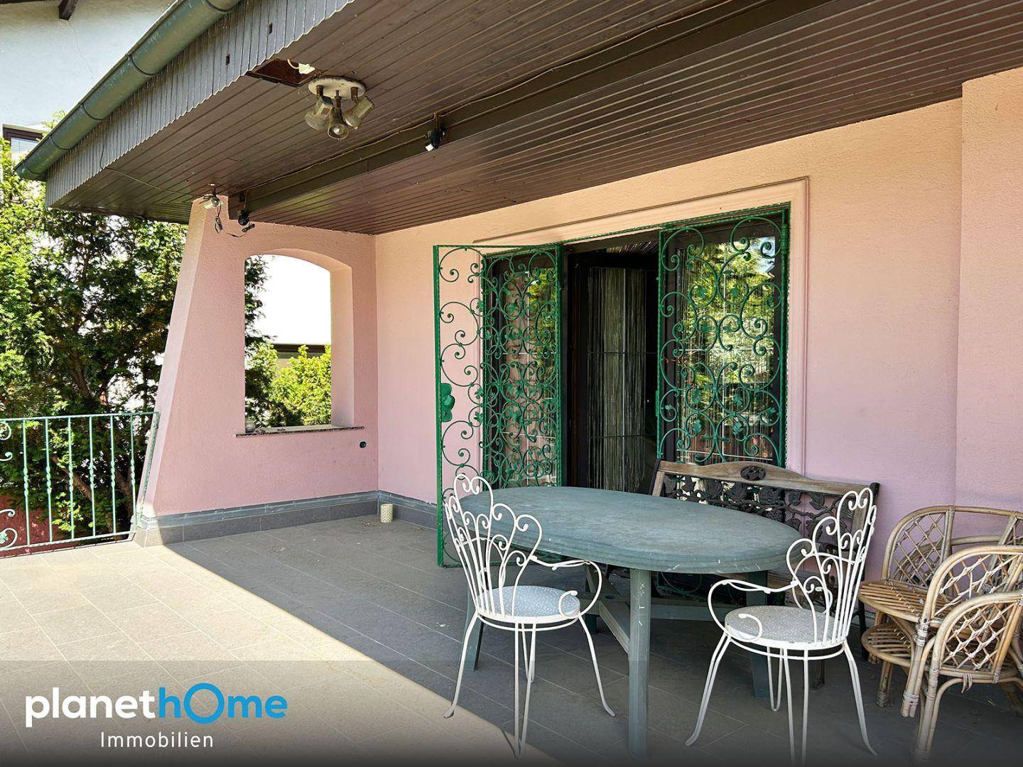 Überdachte Terrasse mit Gartenmöbeln und rosa Fassade.