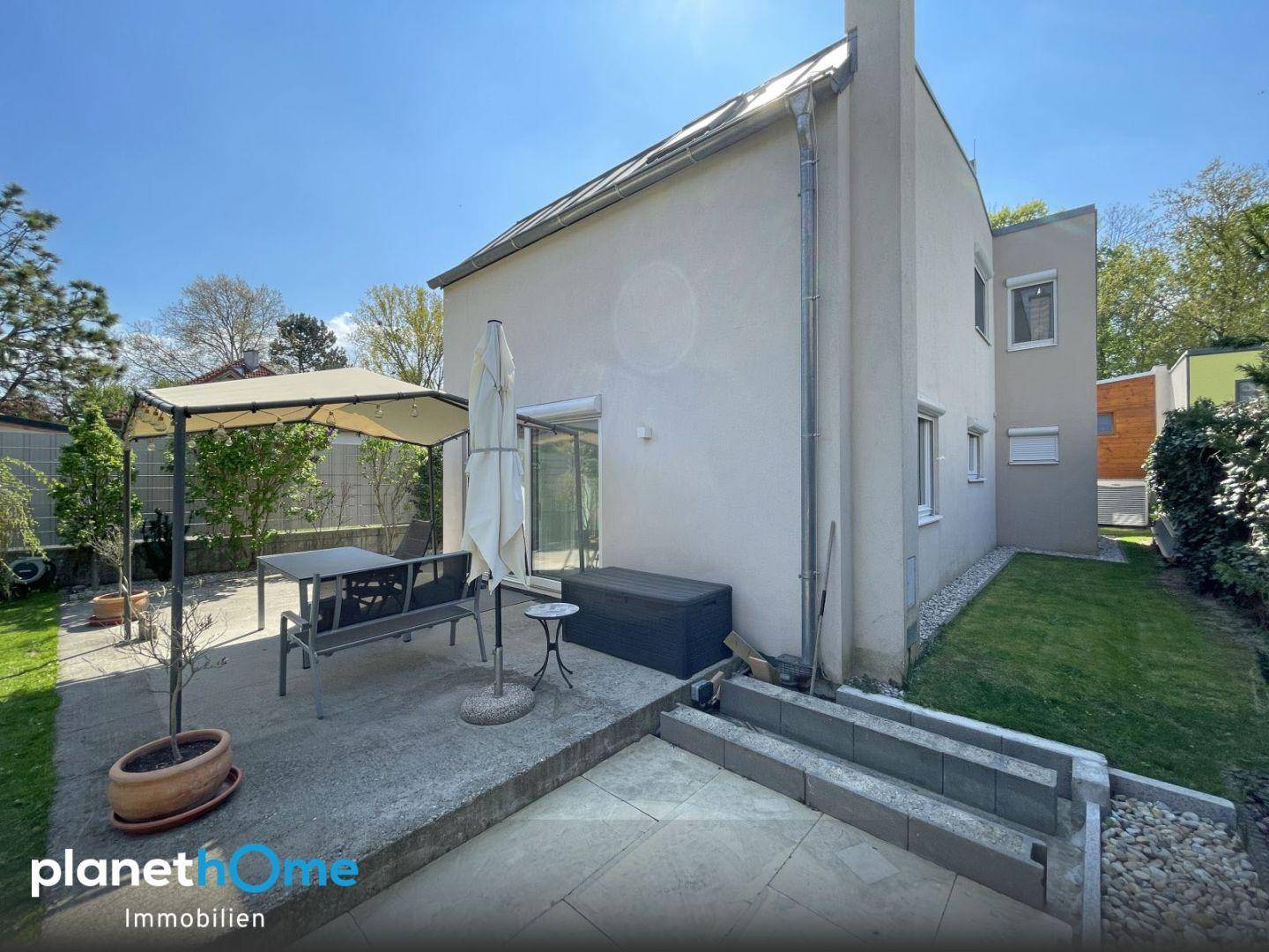 Seitliche Ansicht des Hauses mit einer gepflasterten Terrasse und einem kleinen Gartenbereich.
