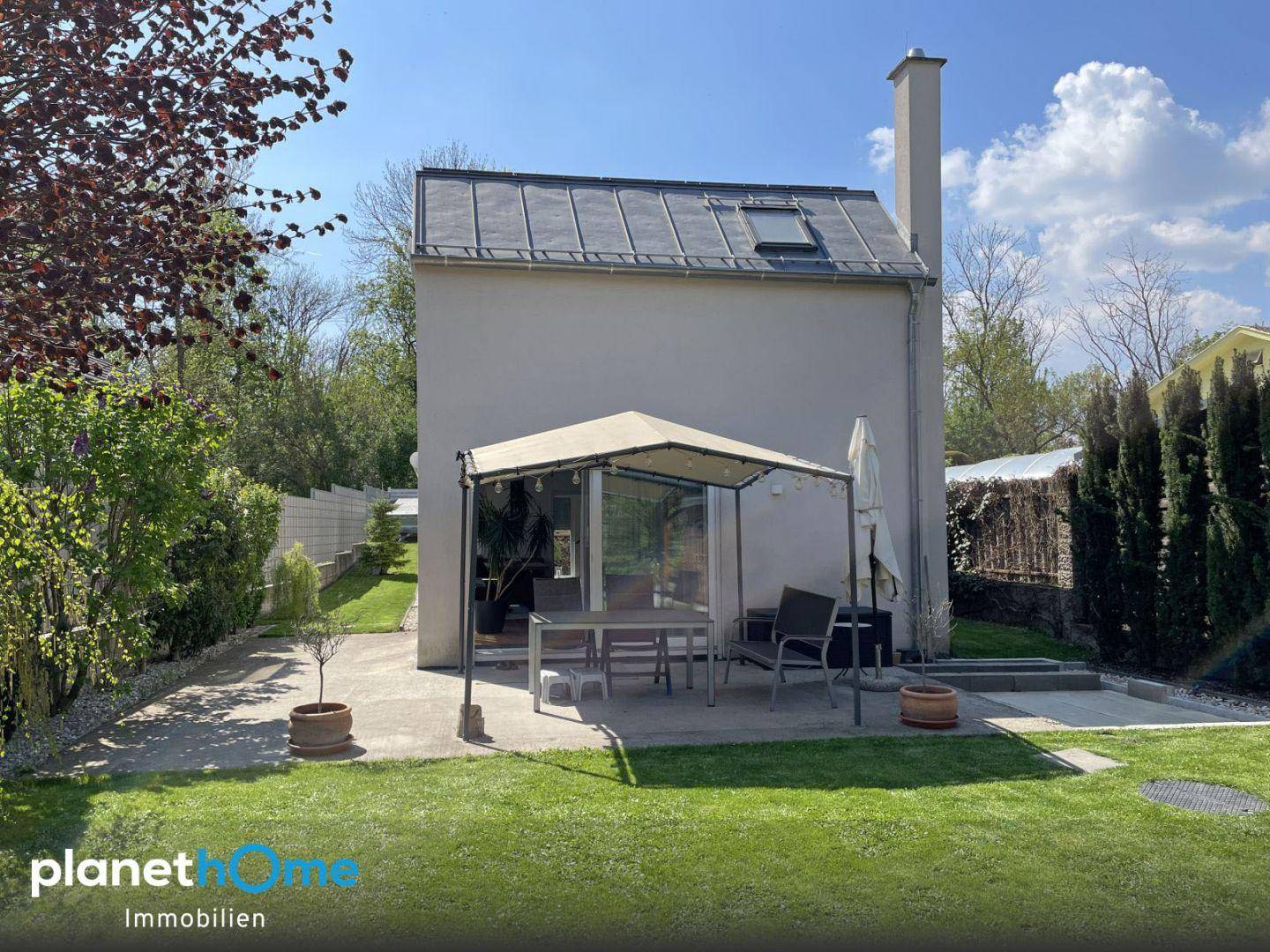 Rückansicht des Hauses mit gepflegtem Rasen und einer kleinen Terrasse mit Sonnenschutz.