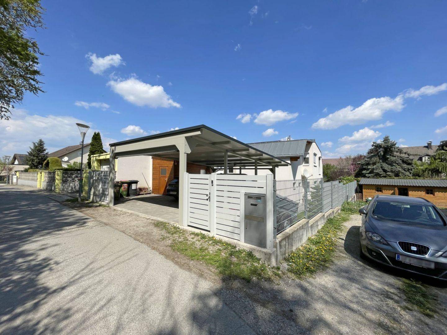 Blick von der Straße auf das Grundstück mit Carport und dem Wohnhaus im Hintergrund.