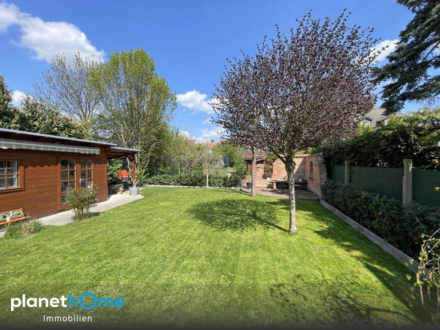 Großer, sonniger Garten mit Rasenfläche, Baumbestand und einem Gartenhaus.