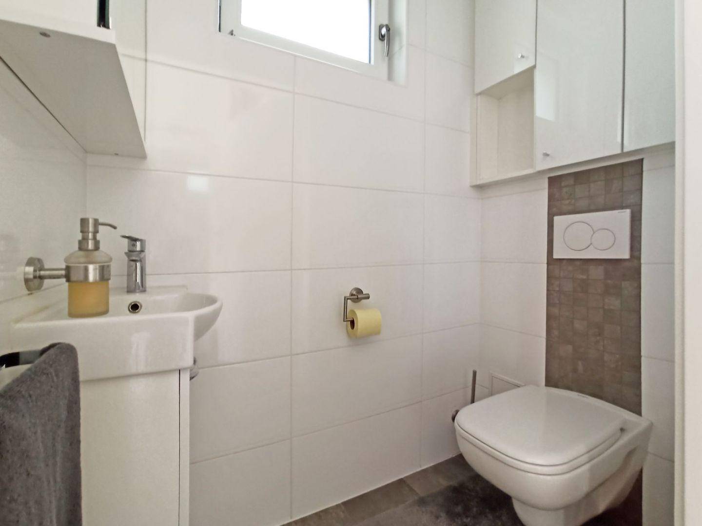 Modernes Gäste-WC mit wandhängendem WC, kleinem Waschbecken und Fenster.