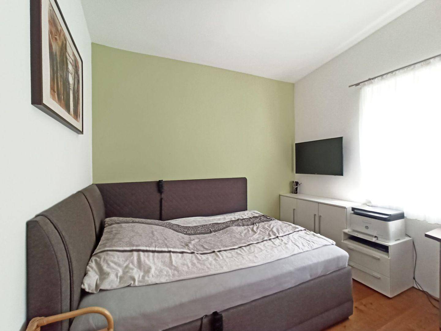 Gemütliches Schlafzimmer mit Doppelbett, grüner Akzentwand und Fernseher.