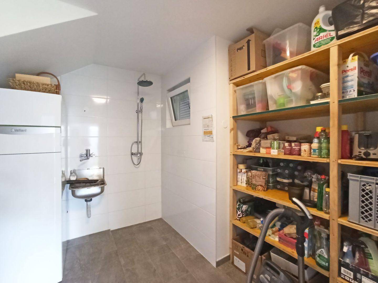 Praktischer Hauswirtschaftsraum mit Dusche, Waschbecken und Regalen für Vorräte.