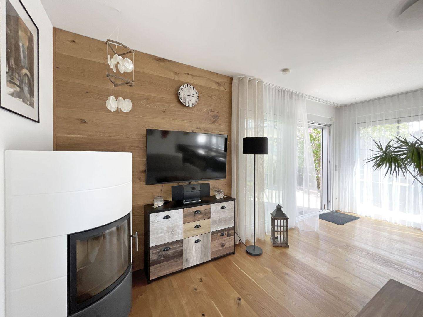 Gemütliches Wohnzimmer mit Kaminofen, Holzwand und Zugang zum Außenbereich.
