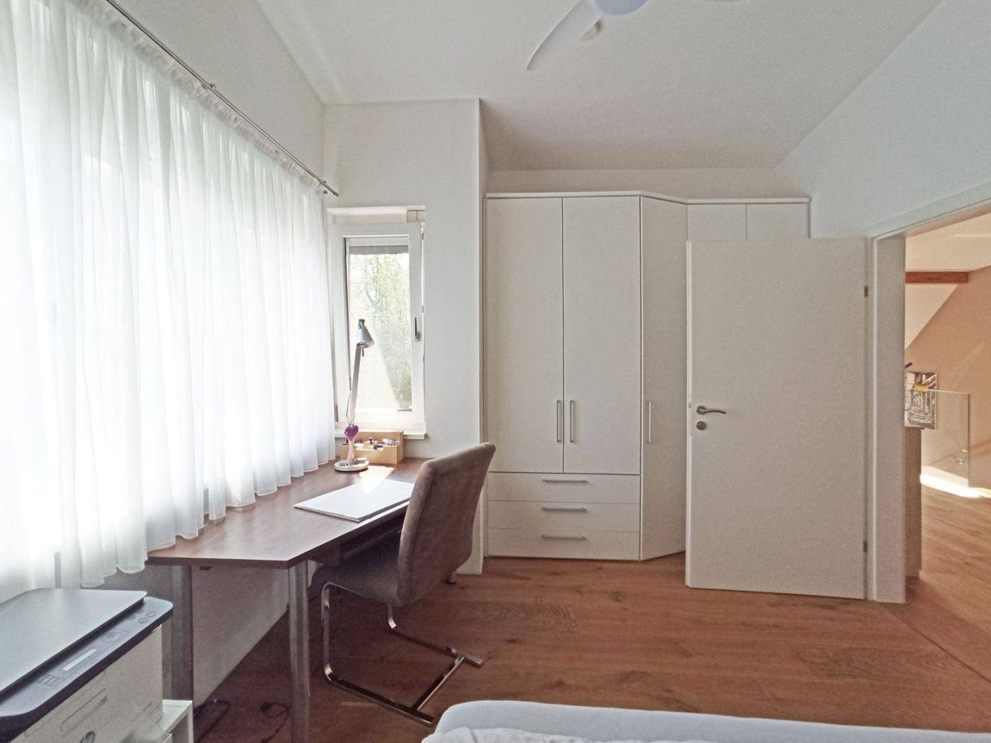 Helles Schlafzimmer mit Schreibtisch, Einbauschrank und großem Fenster.