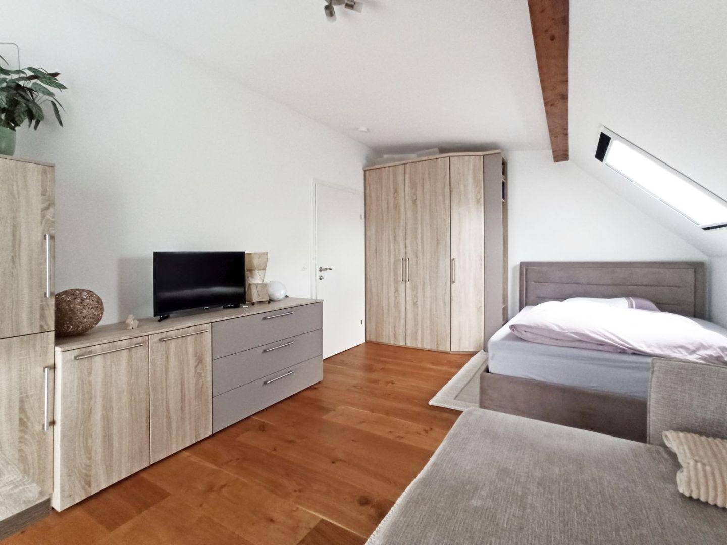 Gemütliches Schlafzimmer mit Dachschräge, Holzbalken, Bett und Kleiderschrank.