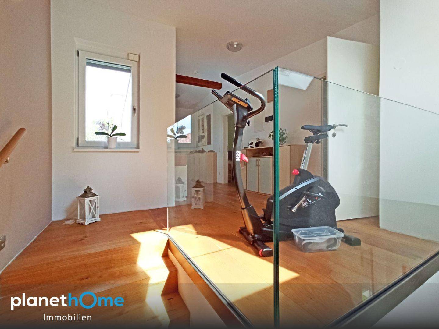 Heller Flurbereich mit Holzfußboden, Glasgeländer und Fitnessgerät.