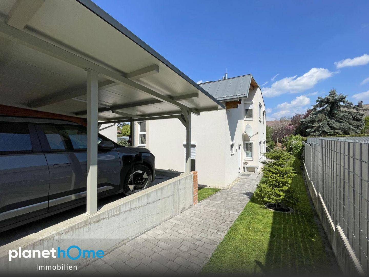 Außenansicht des Hauses mit Carport, Elektrofahrzeug und gepflegtem Vorgarten.