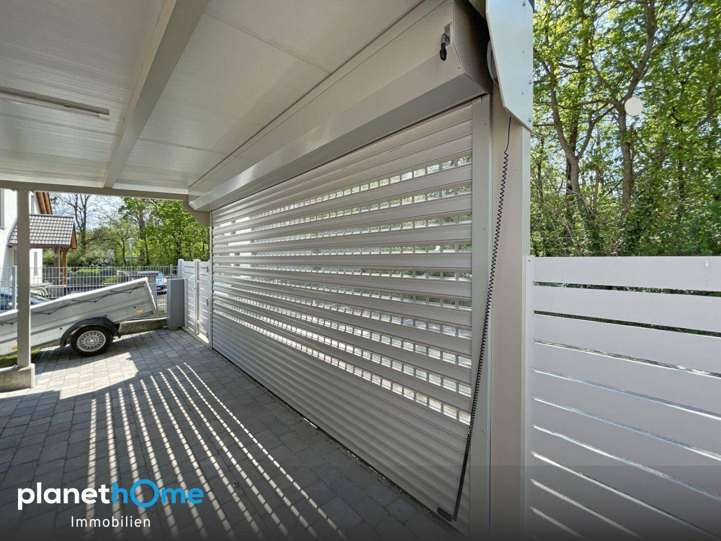 Überdachter Carport mit geschlossenem Rolltor und gepflasterter Einfahrt.