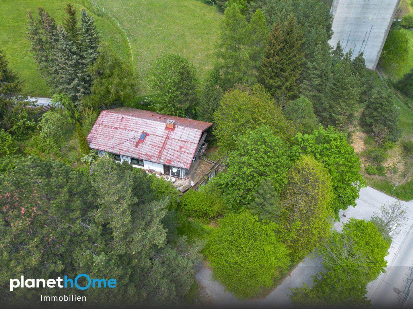 Luftaufnahme des Hauses mit rotem Dach, eingebettet in dichte Wälder und grüne Natur.