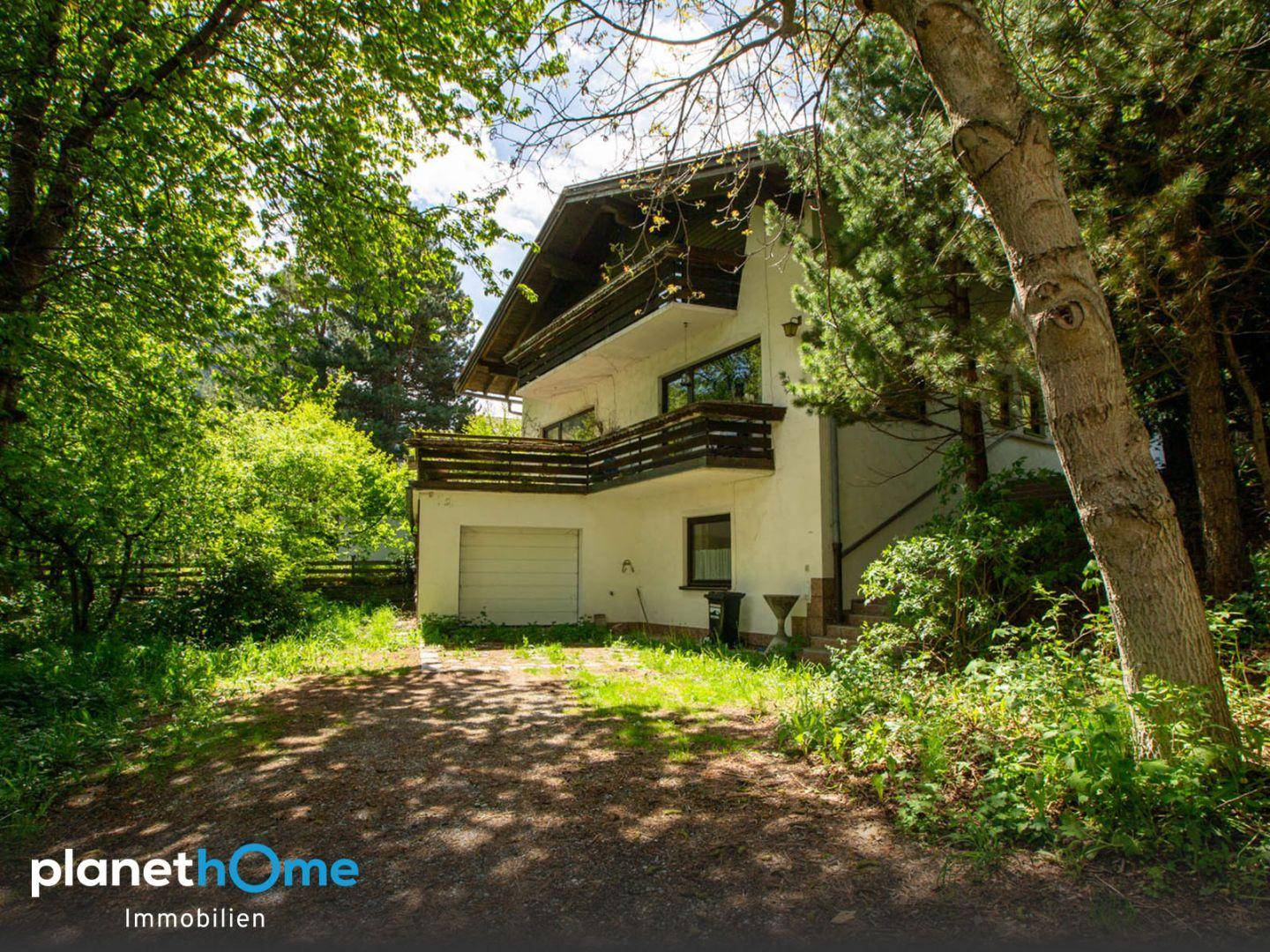 Das Haus von außen, umgeben von Bäumen, mit Balkonen und einer Garageneinfahrt.