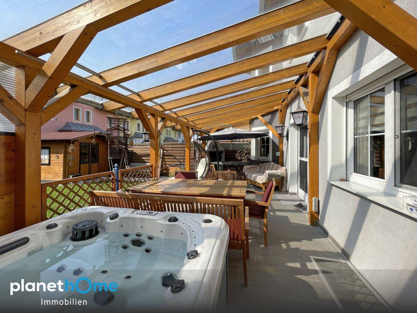 Überdachte Terrasse mit Whirlpool, Esstisch und Holzpergola, ideal für Entspannung und Mahlzeiten im Freien.