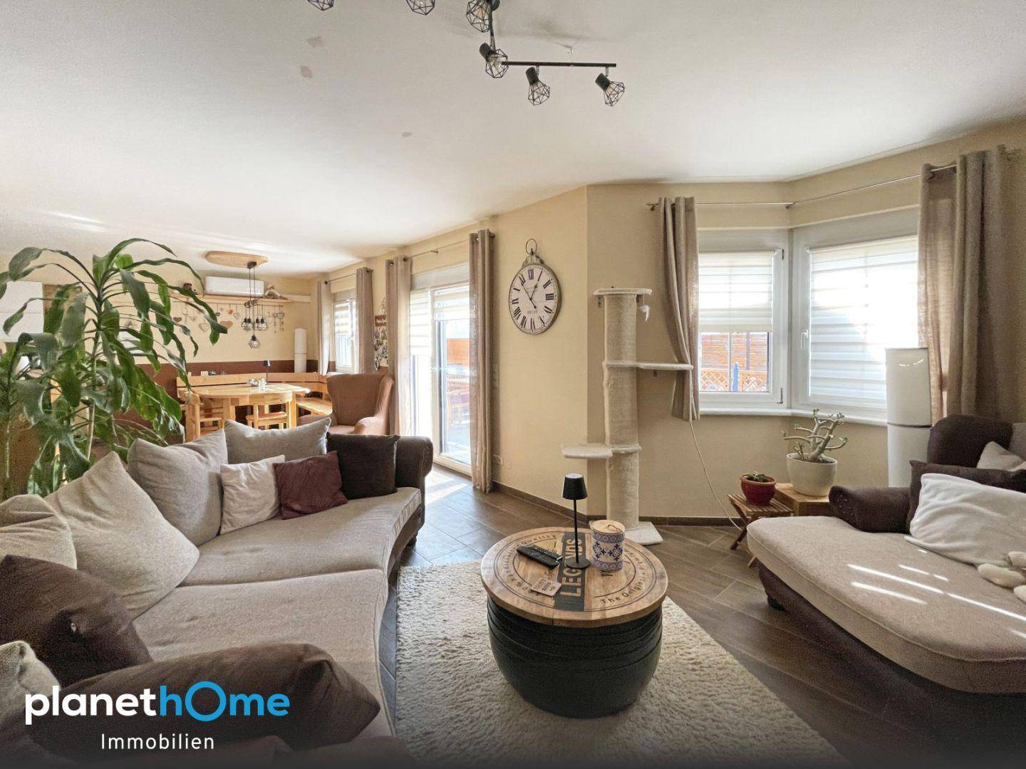 Gemütliches Wohnzimmer mit großem Sofa und angrenzendem Essbereich, hell durch Erkerfenster.
