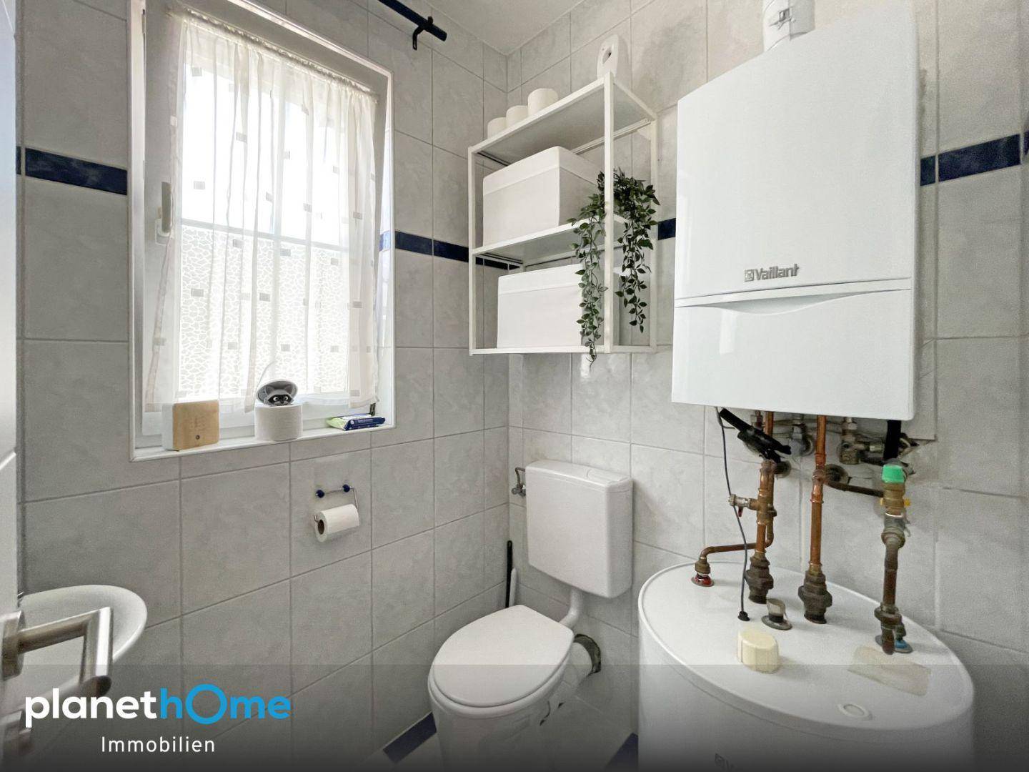 Kleines Badezimmer mit WC, Waschbecken und Fenster, inklusive Warmwasserbereiter.