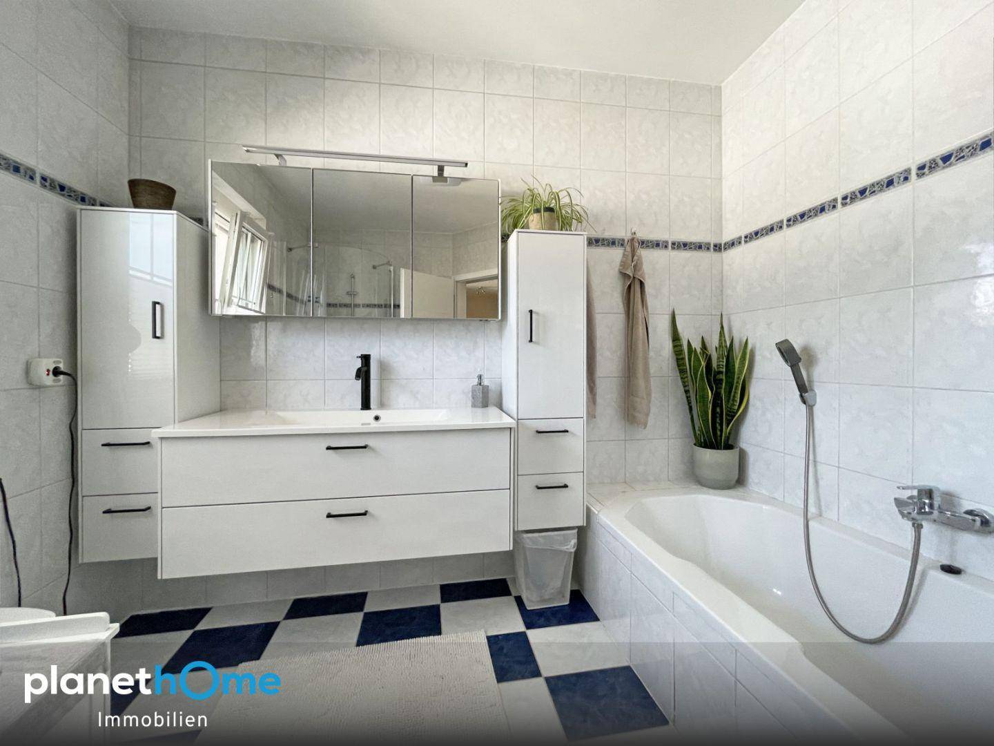 Badezimmer mit modernem Waschtisch, Spiegelschrank und Badewanne, hell gefliest.